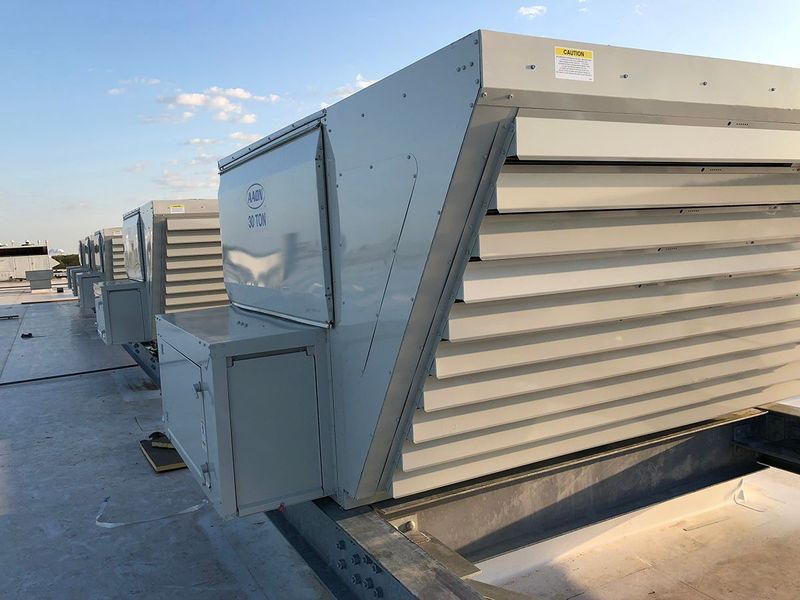 A row of industrial rooftop ventilation units with sloped, louvered air intakes under a clear, bright blue sky.