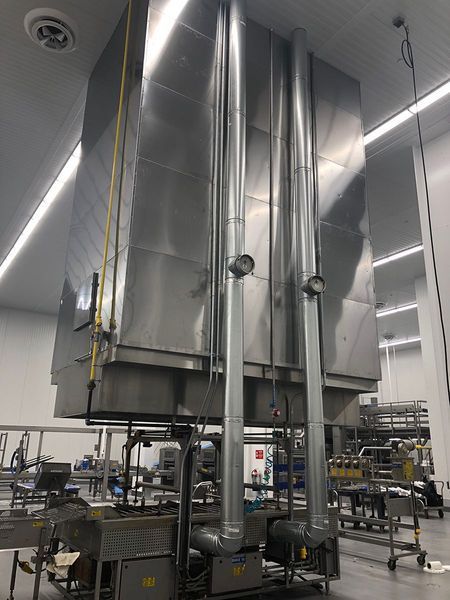 Large stainless steel industrial ventilation hood suspended over production equipment in a manufacturing facility.