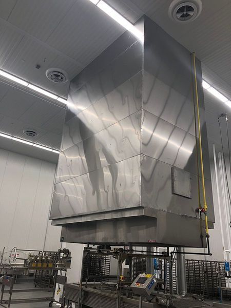 A large industrial stainless steel ventilation hood suspended over kitchen equipment in a commercial space.