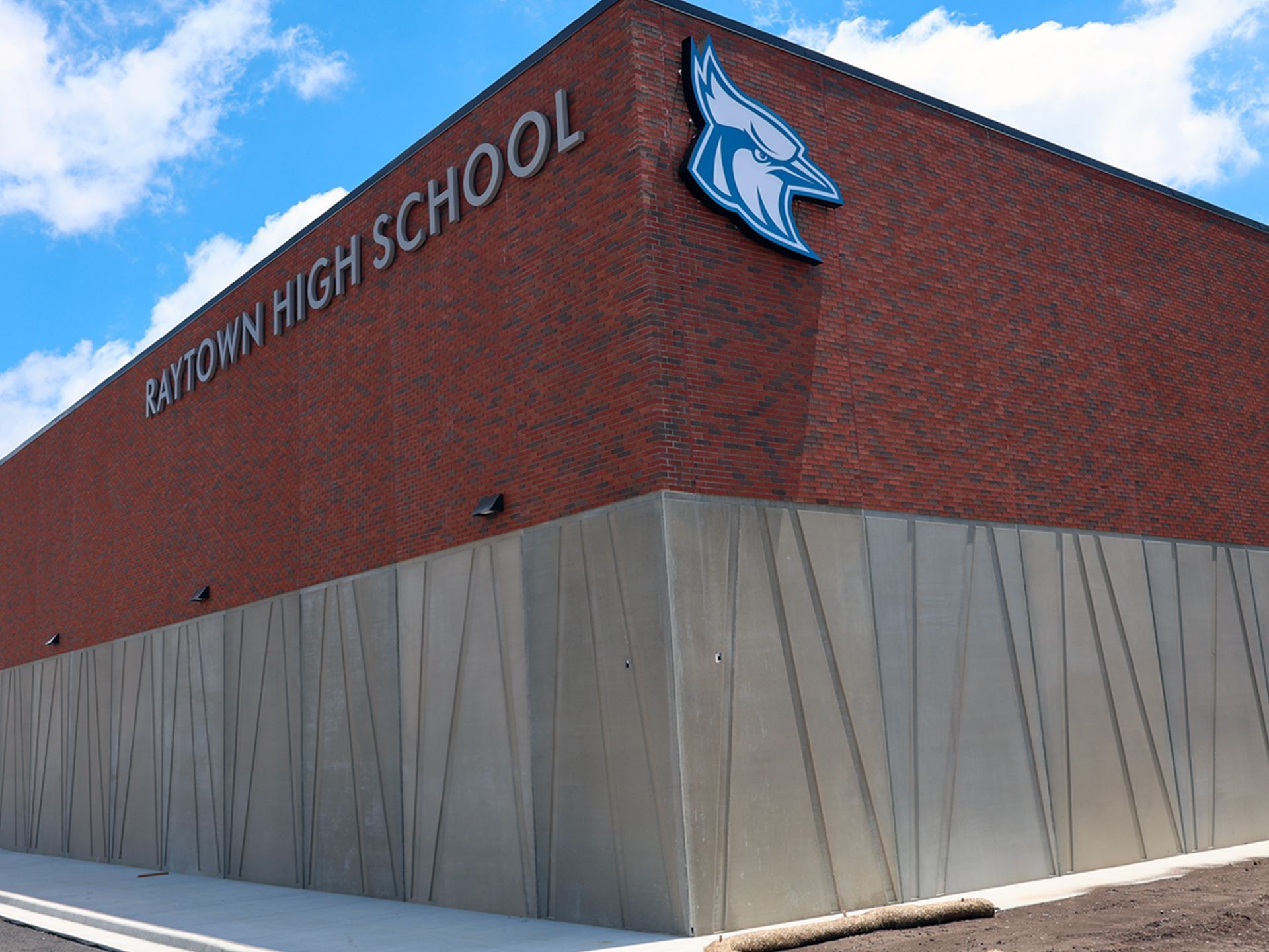 A corner of Raytown High School with a red brick exterior, a blue bird mascot logo, and angular metal wall paneling.
