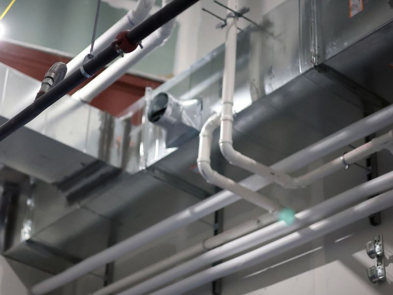 An indoor view looking up at HVAC metal ductwork, white PVC piping, and a black pipe suspended from a ceiling.