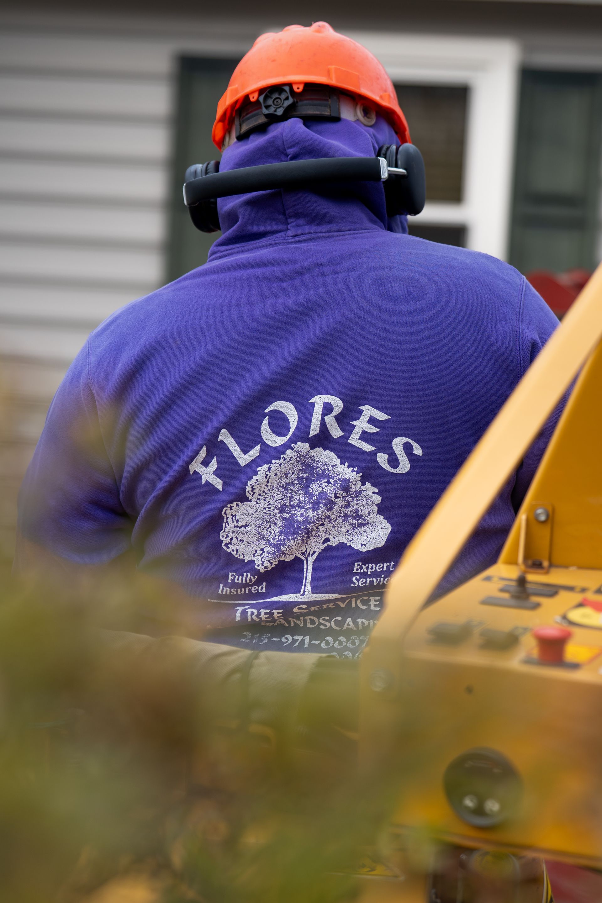 Worker in orange hard hat and purple jacket seen from behind near yellow machinery outdoors