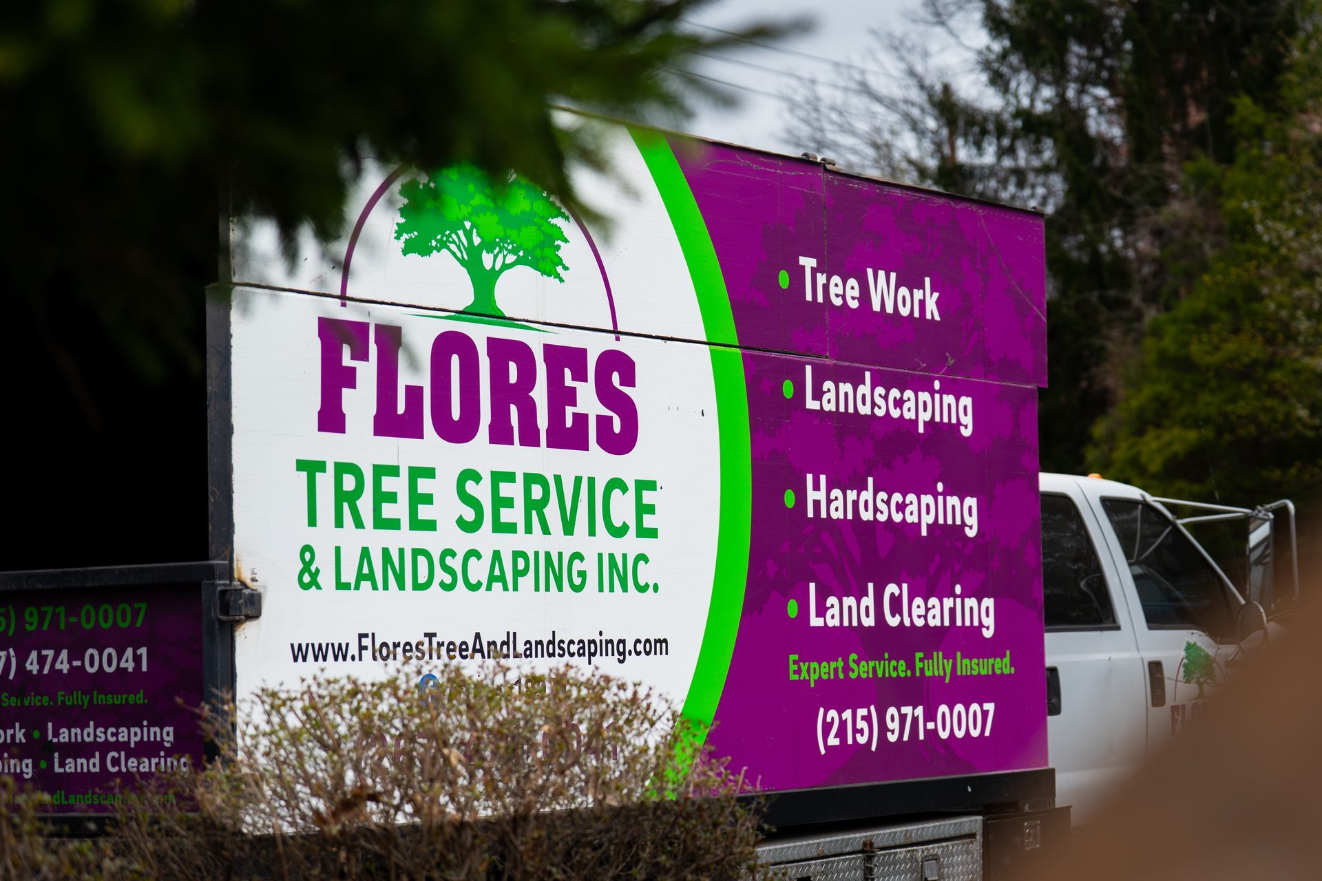 Flores Tree Service and Landscaping sign with purple and white text beside a road