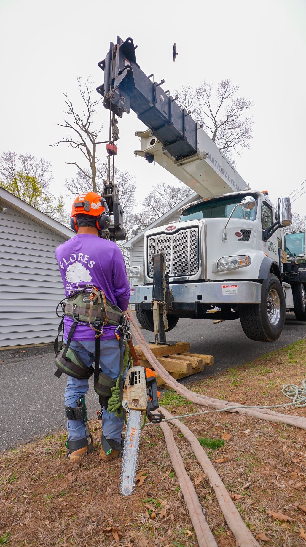 Utility worker in orange helmet stands by a bucket truck handling cables near a house.