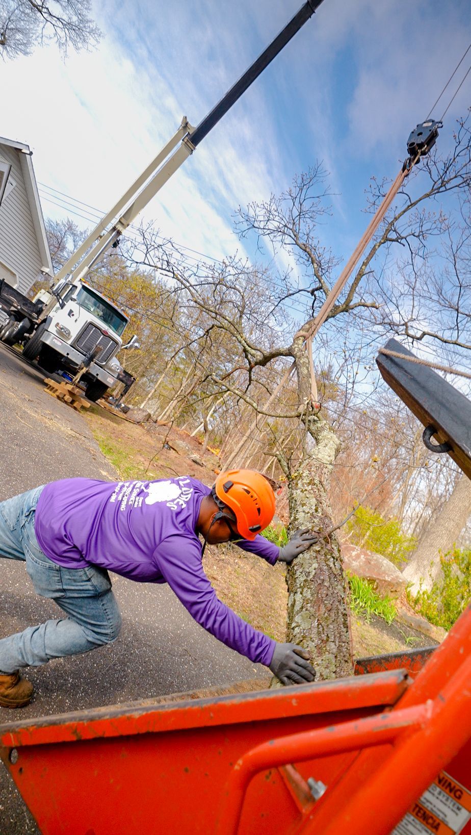 Worker in purple jacket and orange helmet pries at a large rock beside orange machinery on a steep hillside.