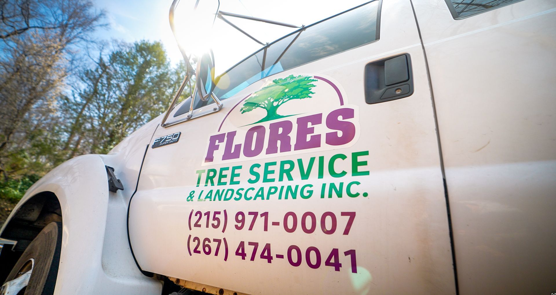 White truck with “Flores Tree Service & Landscaping” logo, phone numbers, and tree graphic on the door.