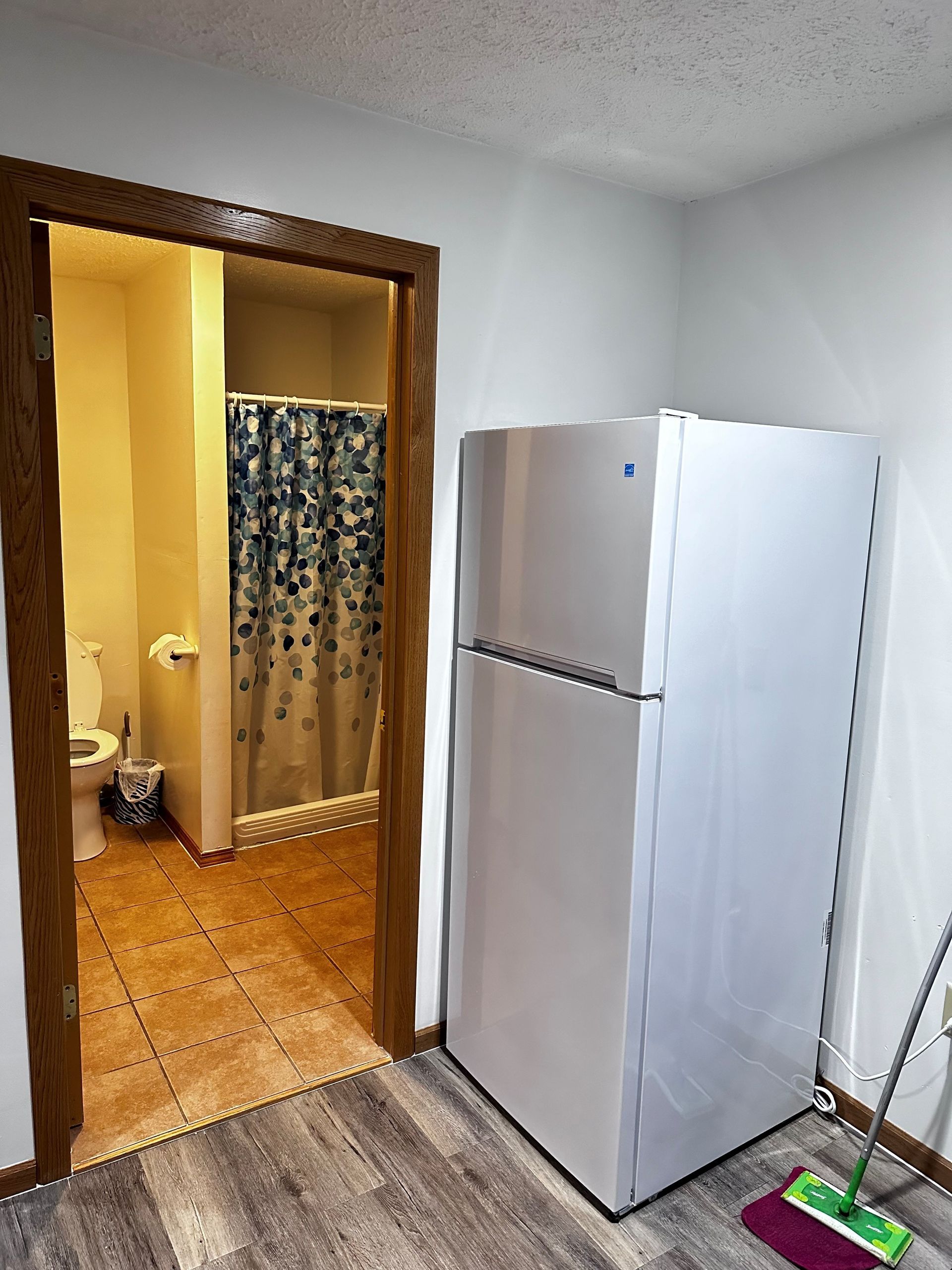 A bathroom with a refrigerator and a mop in it