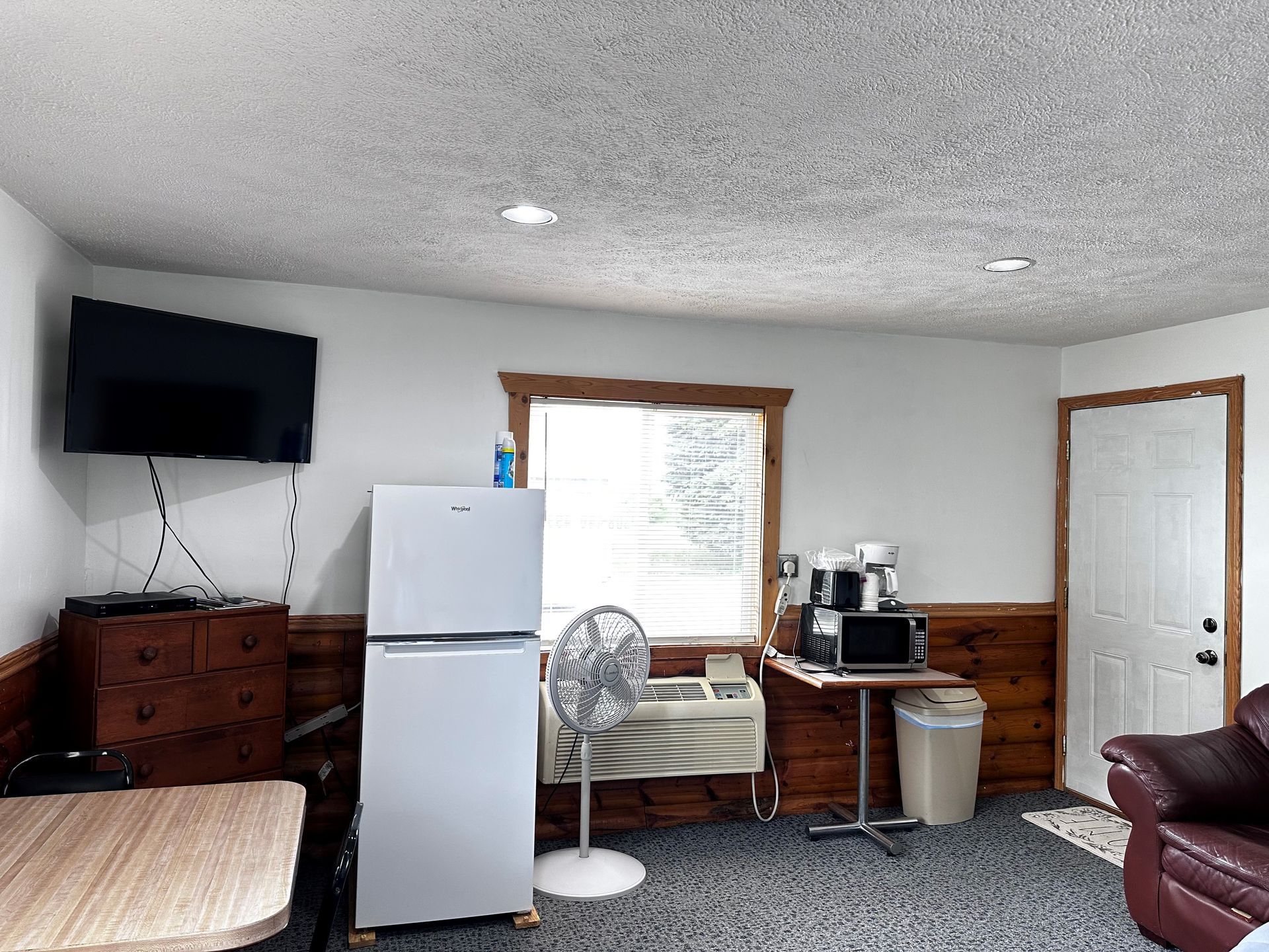A living room with a refrigerator , television , fan , table and chairs.