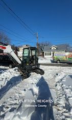 A white and black excavator parked on a snow-covered street in Clifton Heights, Delaware County.