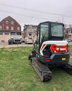 A white and black Bobcat compact excavator parked on a grassy lot in front of a residential street.