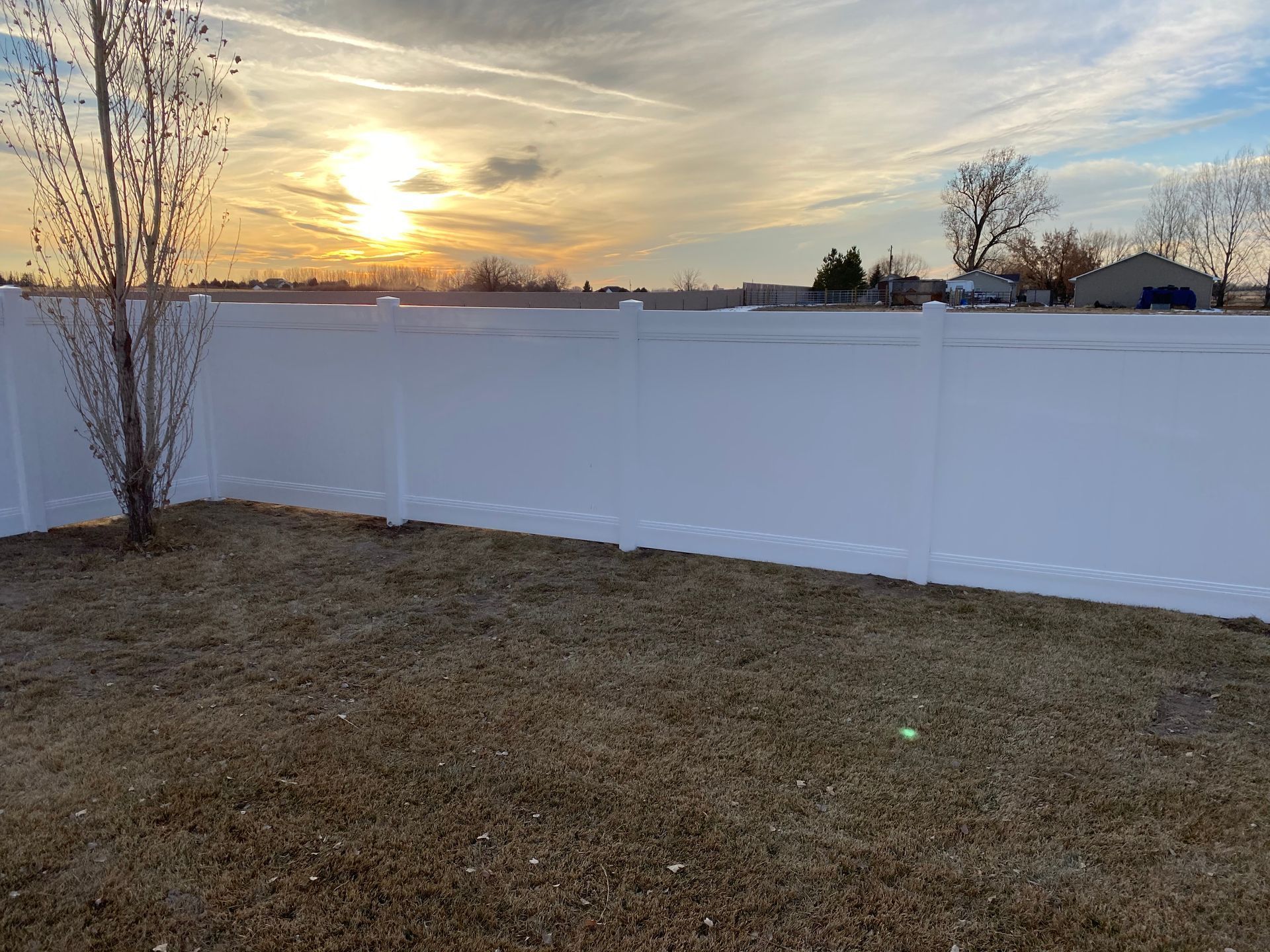 White fence in front of dry grass with a sunset in the background.