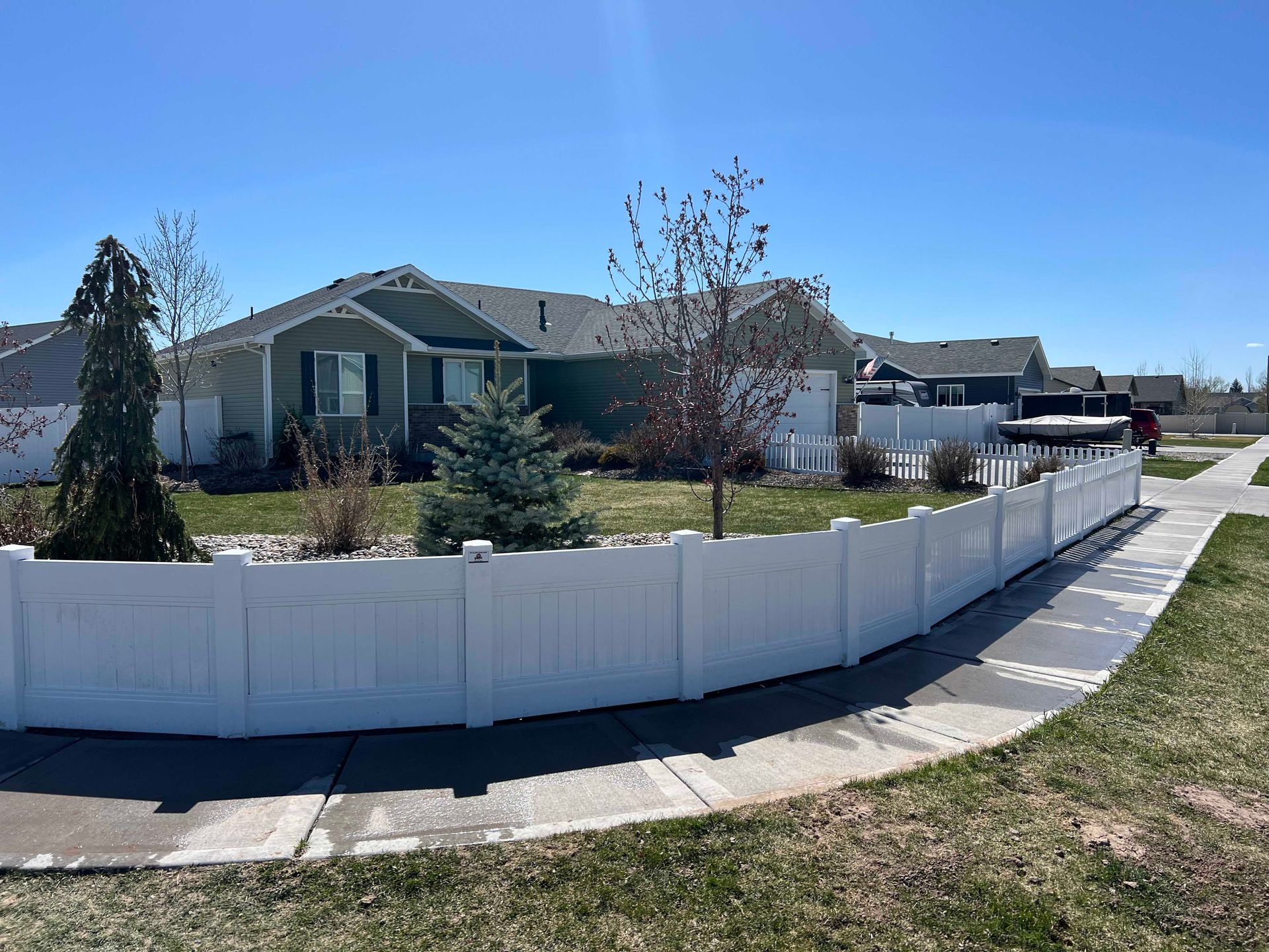 White fence surrounds a green house with a small lawn, under a clear blue sky.