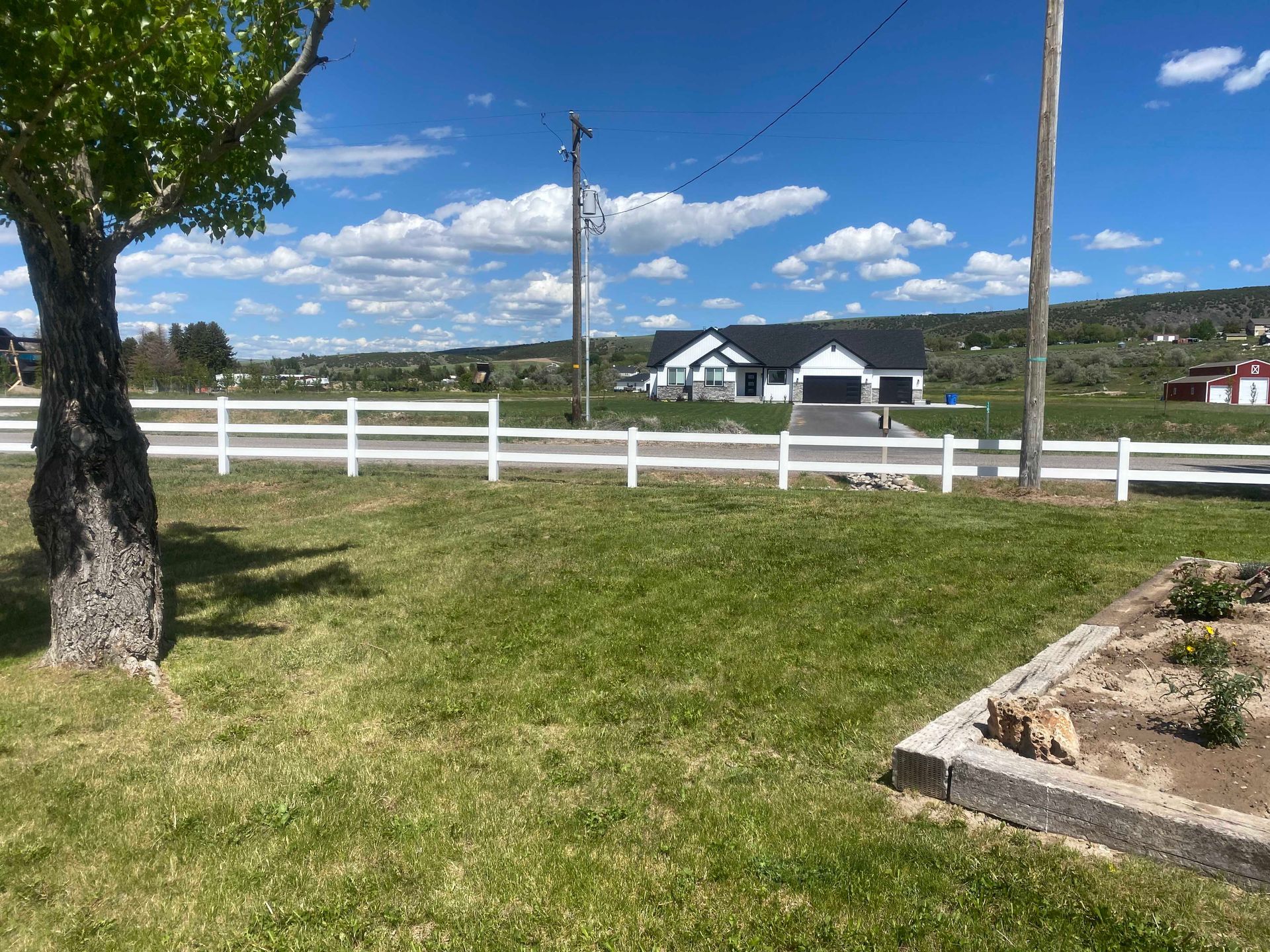 White fence and green lawn in front of a modern house under a blue sky.