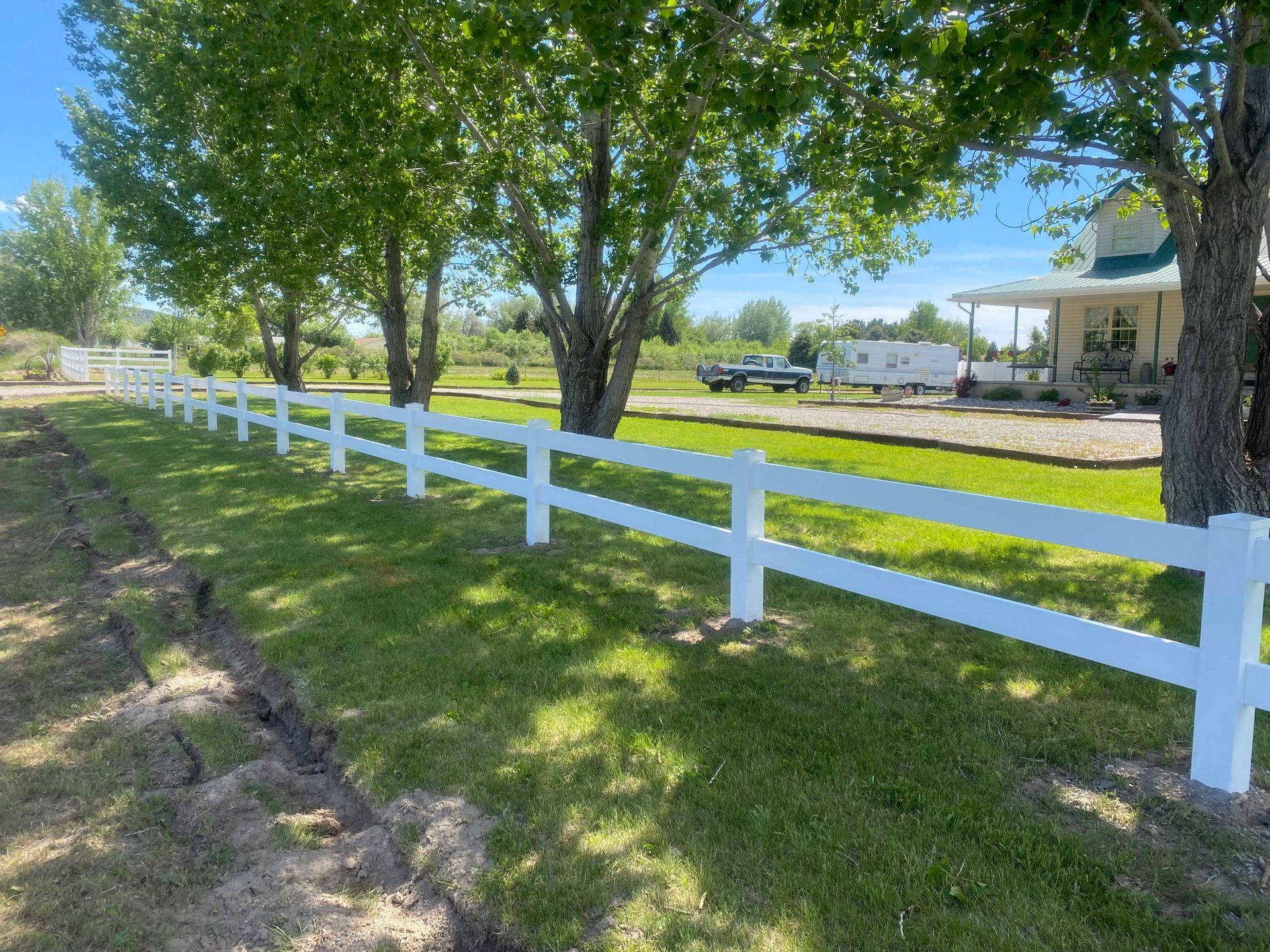 White fence lining a grassy yard, trees in the background, sunny day.