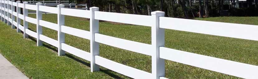 White, three-rail fence alongside a grassy lawn with a sidewalk.