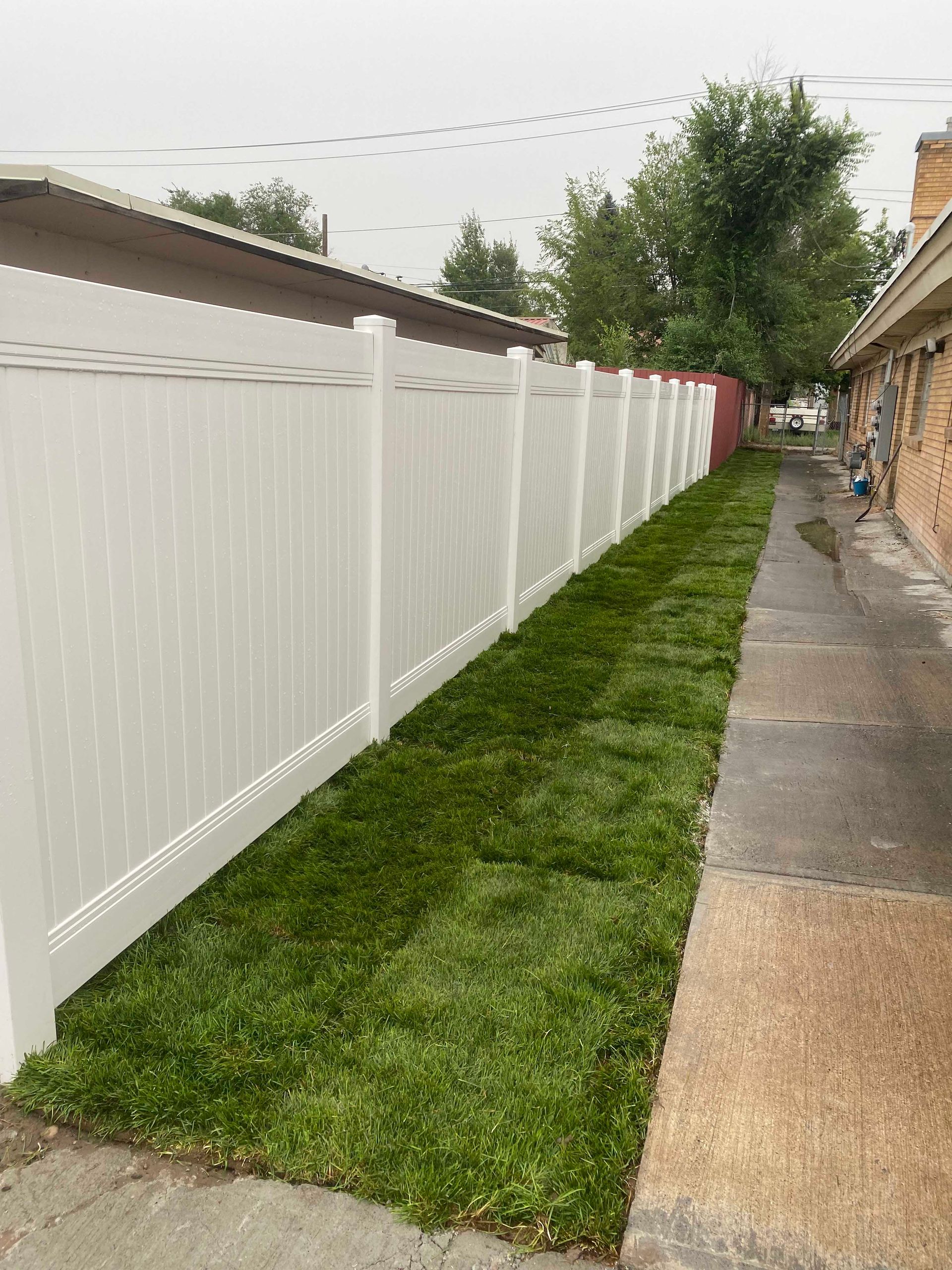 White fence alongside a strip of green grass and a concrete walkway.