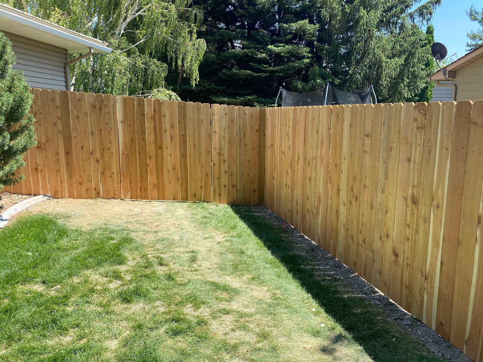 Wooden fence surrounds a patch of green grass in a yard on a sunny day.