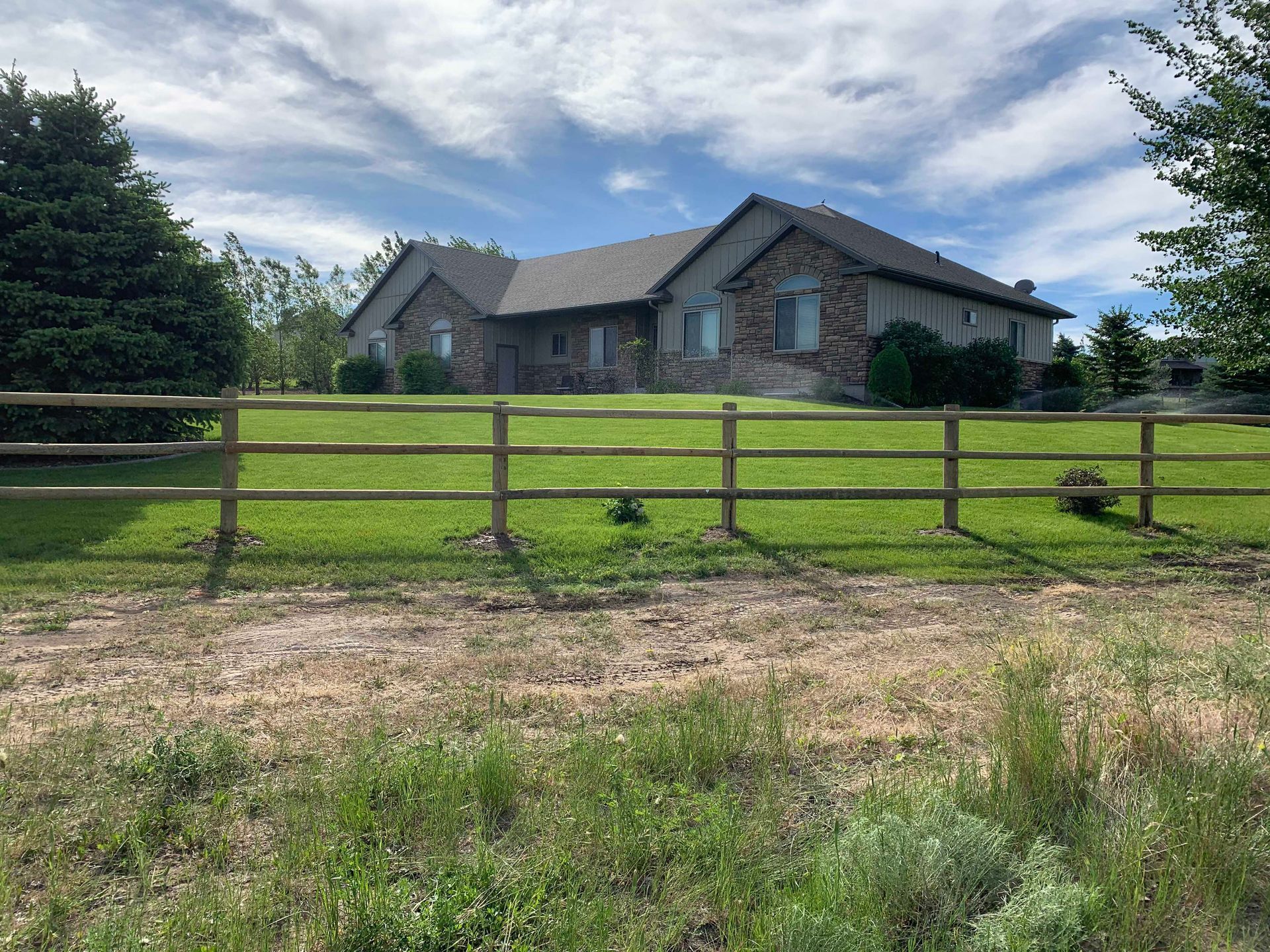 A house behind a split-rail fence on a sunny day with a blue and cloudy sky.