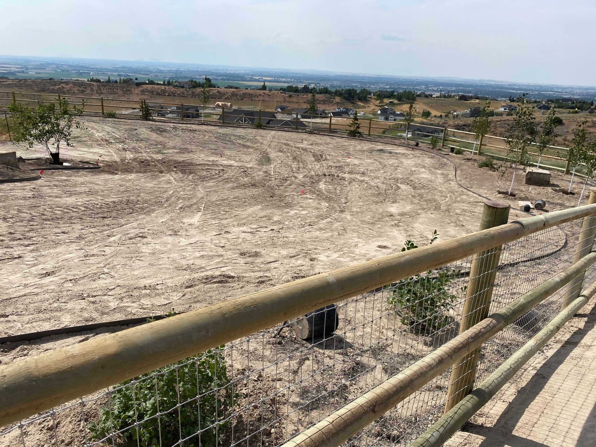 Wooden fence overlooking a dirt landscape with sparse trees and a distant city skyline.
