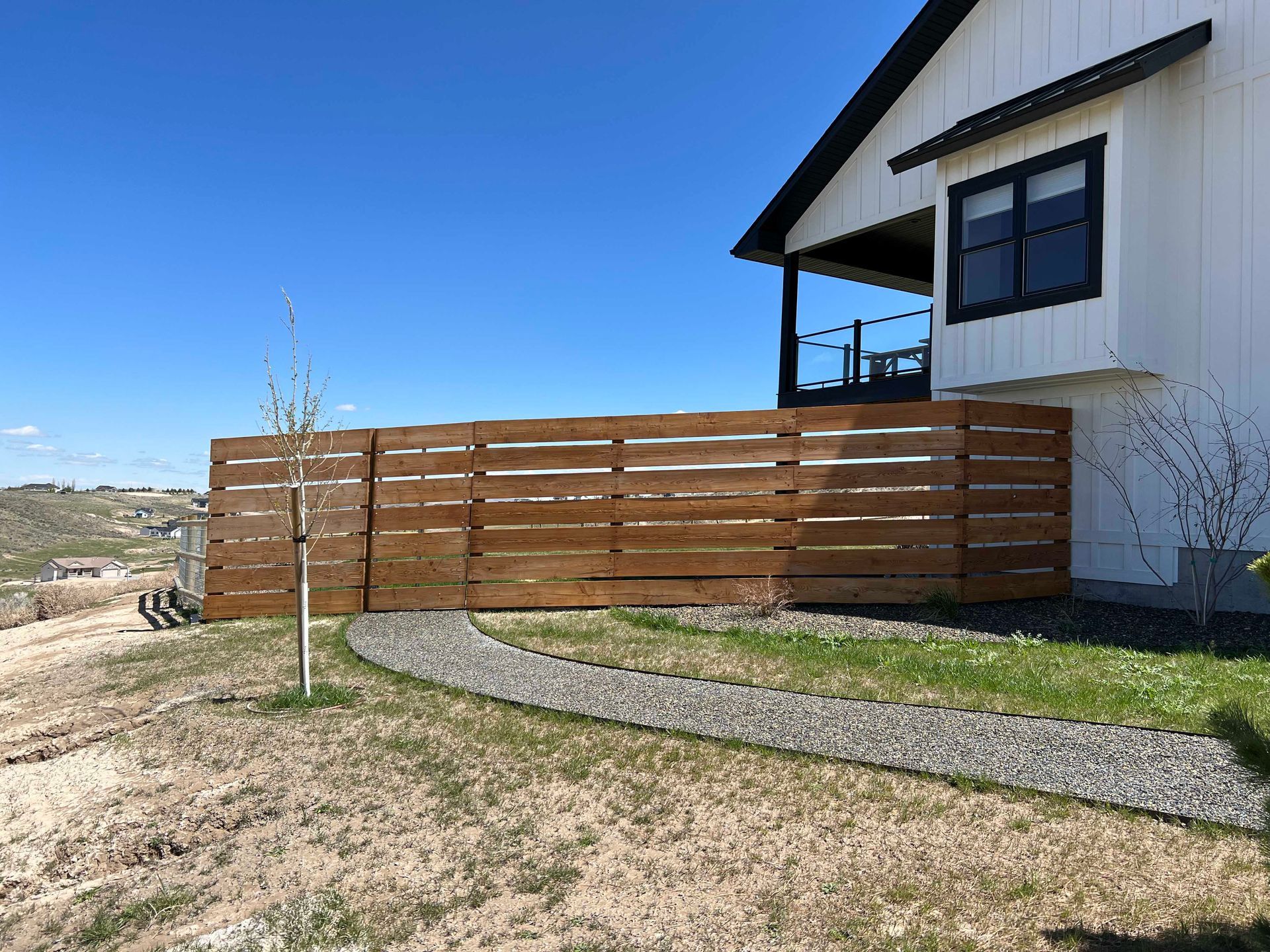 A brown wooden fence surrounds a house with a gravel pathway in a yard.