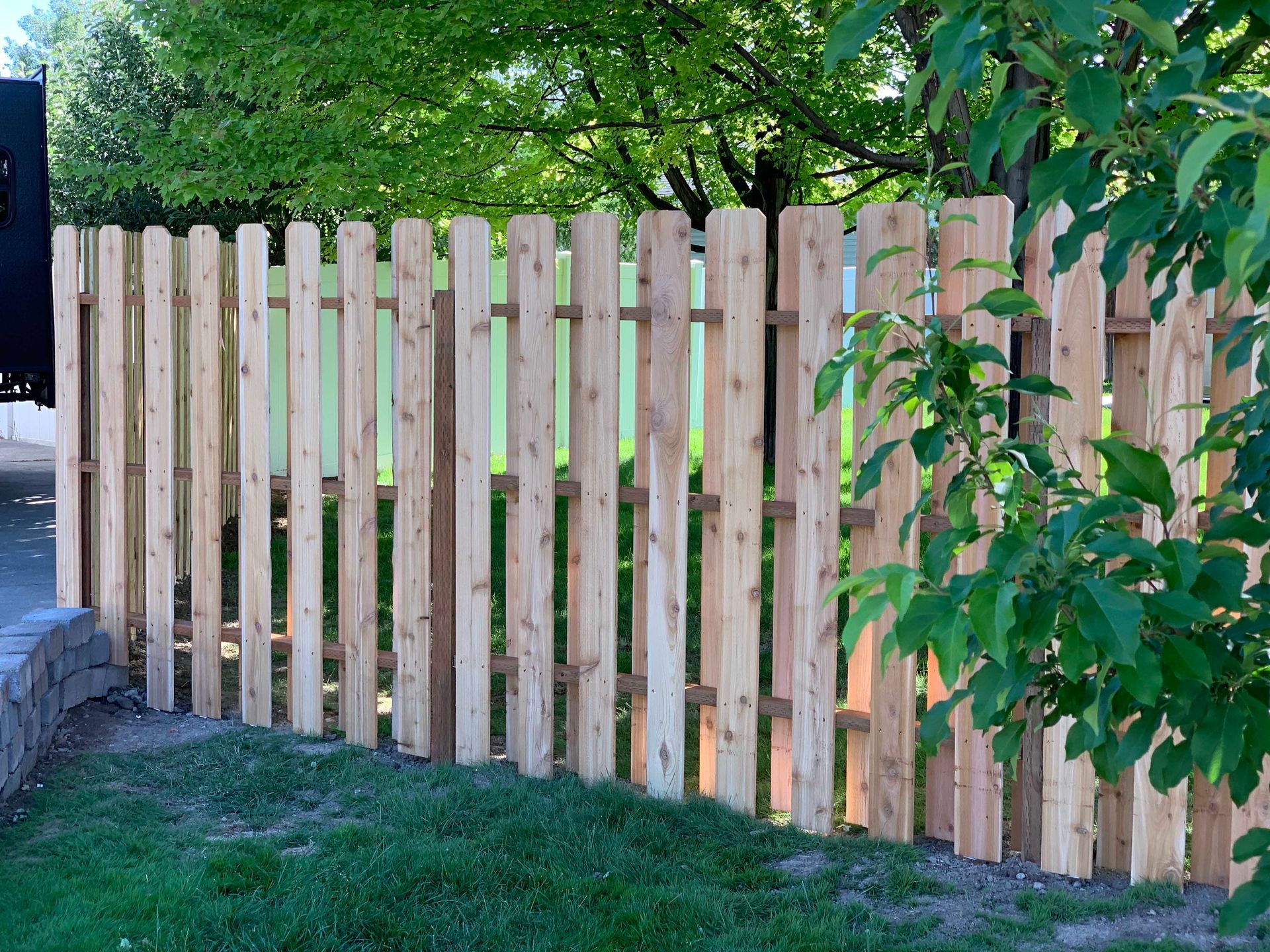 Wooden picket fence surrounding a grassy yard with a tree in the background.