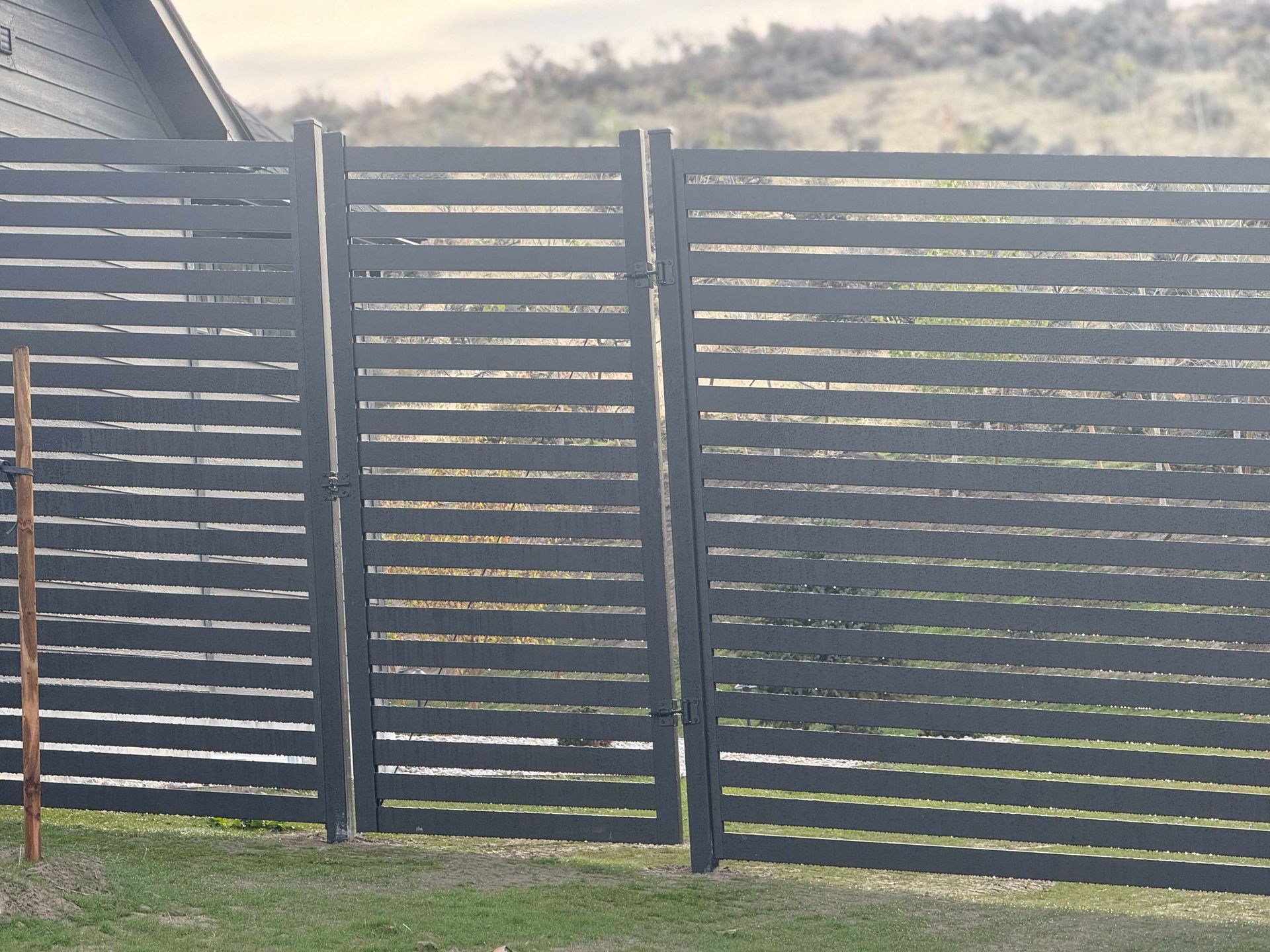 Dark gray horizontal slat fence with gate on green grass. Hills in background.