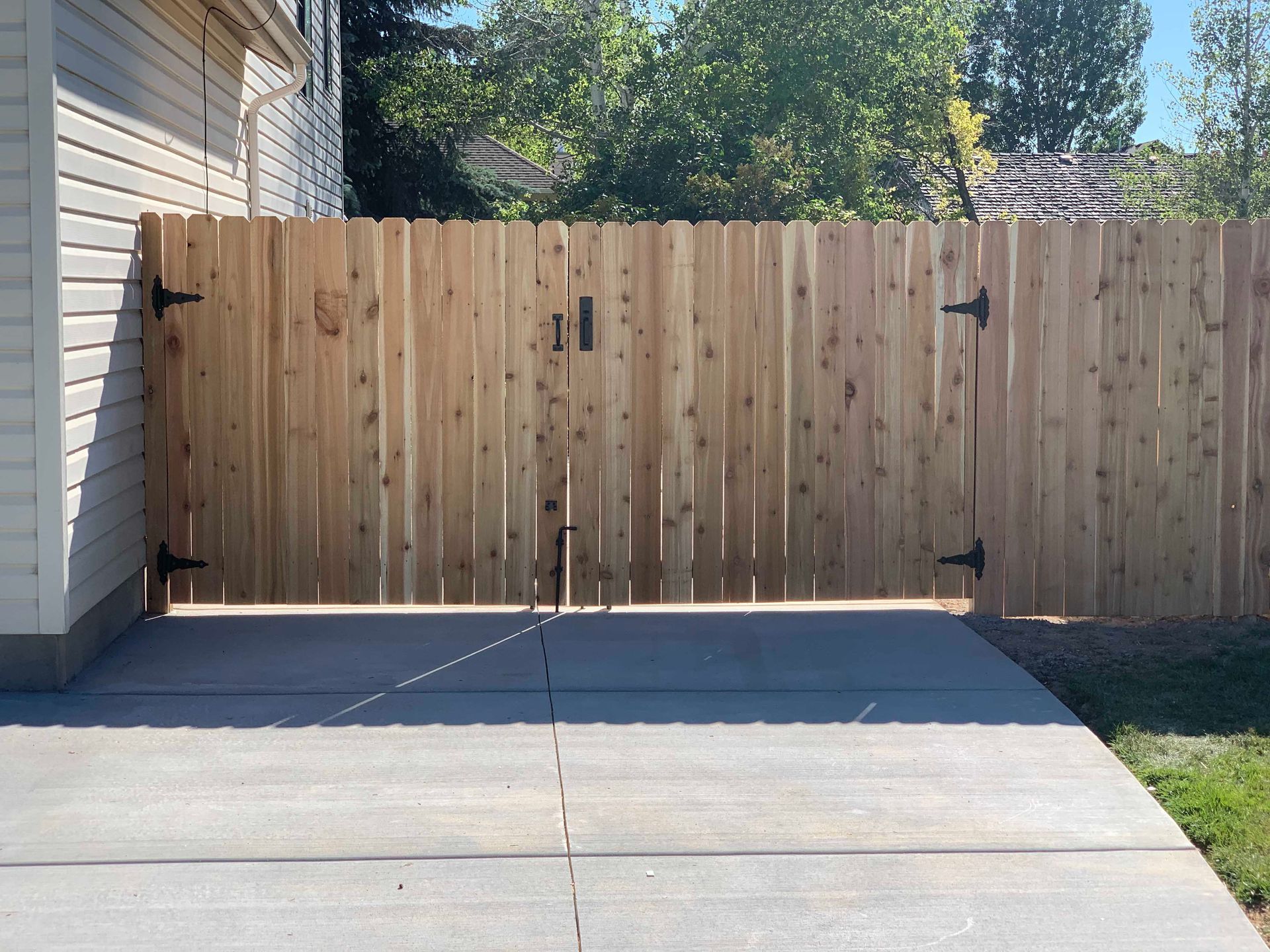 Wooden double gate in a wooden fence on a concrete driveway.
