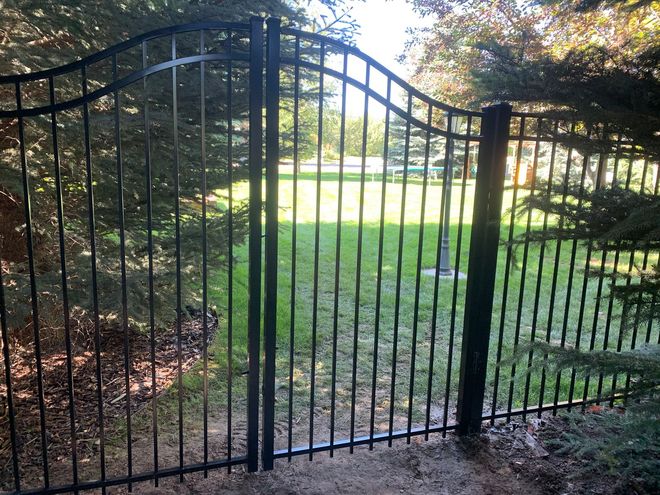 Black wrought iron gate in front of a green lawn and trees.