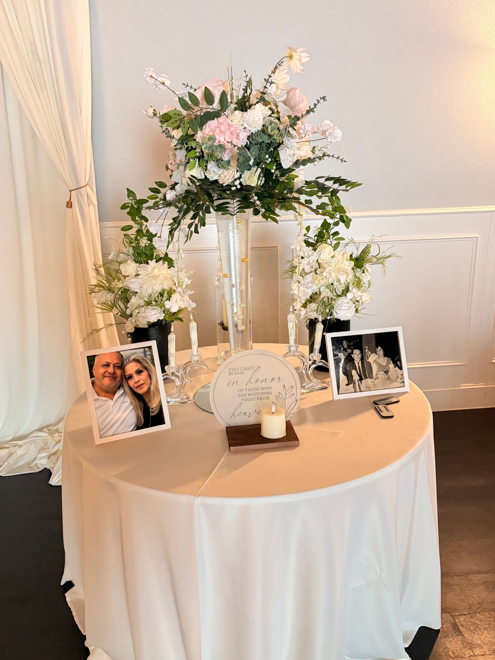 Wedding reception table with floral arch, framed photos, and a white candle centerpiece