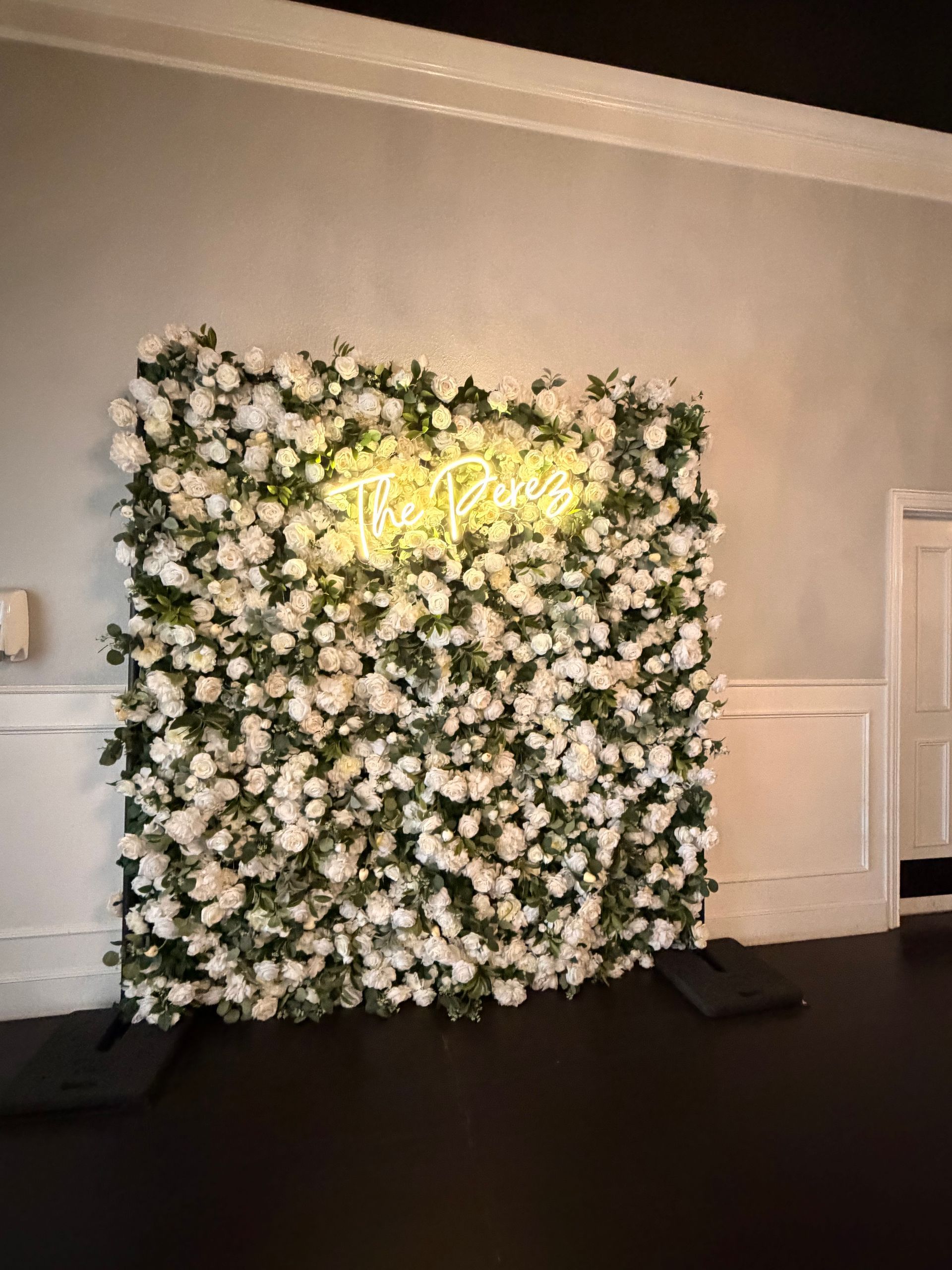 Floral backdrop wall with white flowers and glowing yellow sign in a room