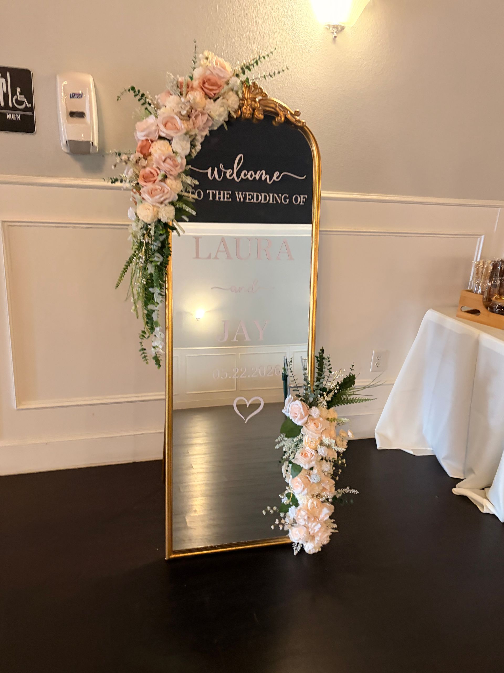 Decorative gold-framed mirror with floral garland and heart decal at a wedding reception entrance