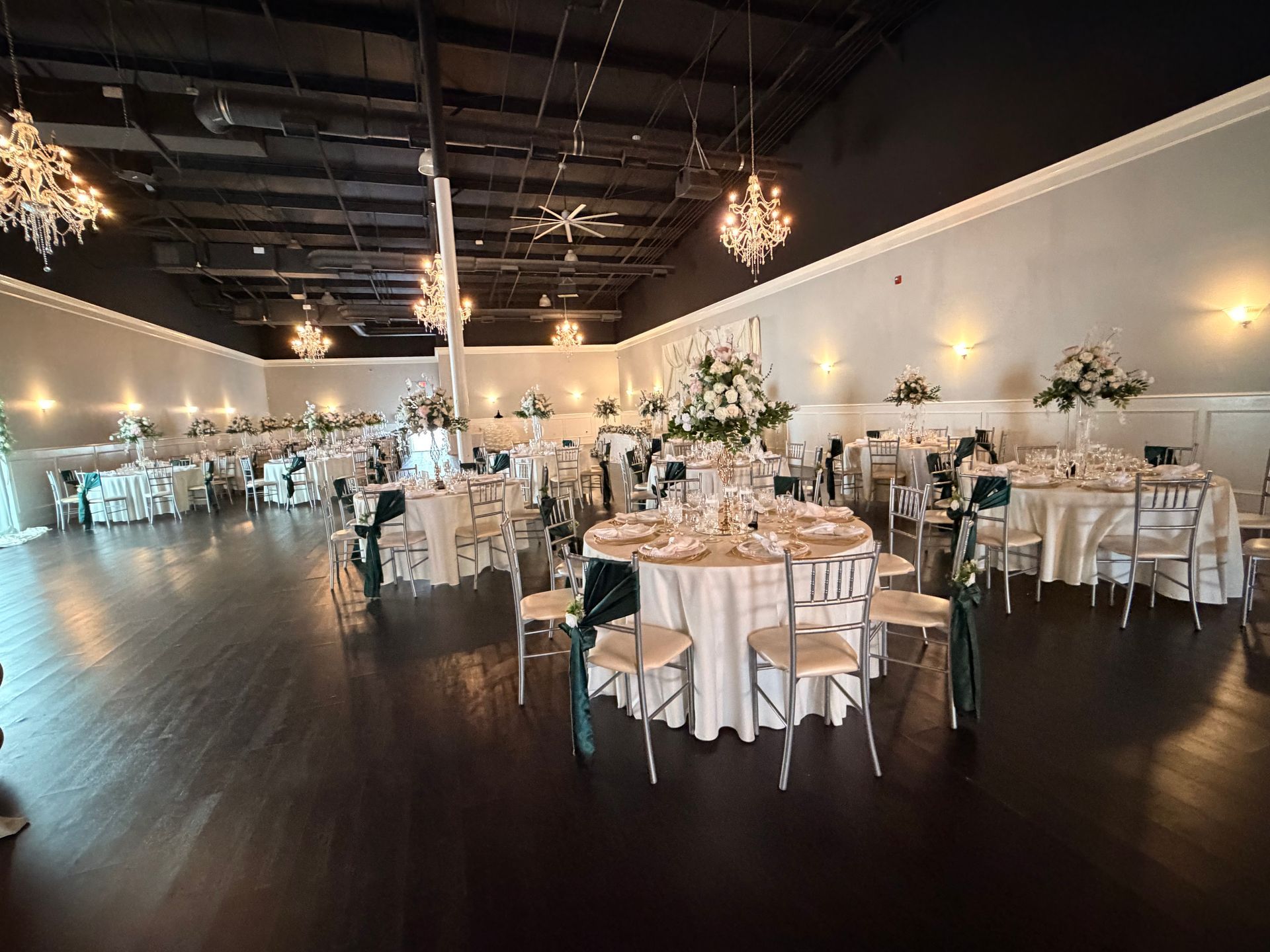 Elegant banquet hall with round tables, white linens, gold chairs, and chandeliers in a dark-ceilinged venue
