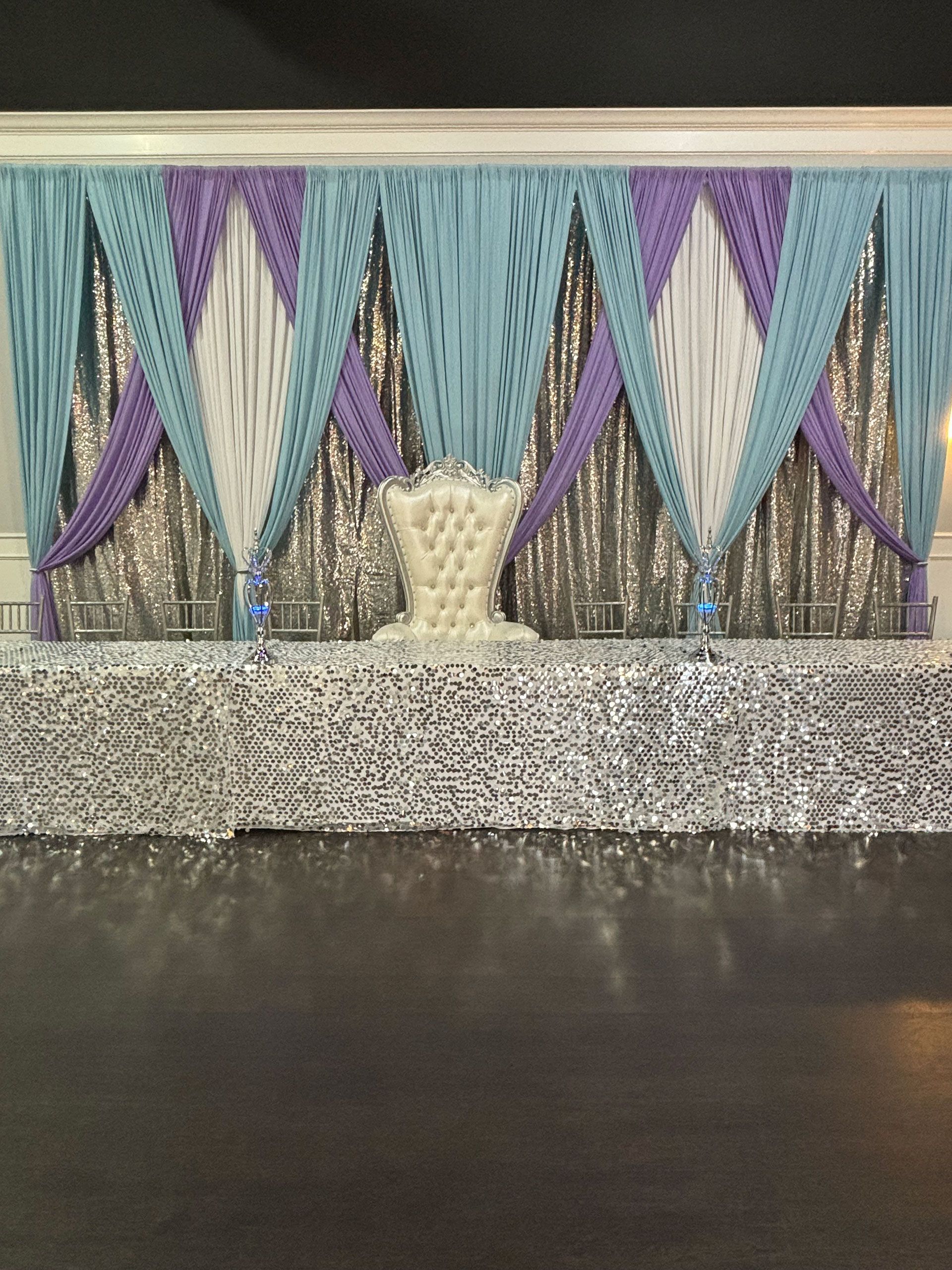 A stage with purple, blue, and silver curtains and a white chair