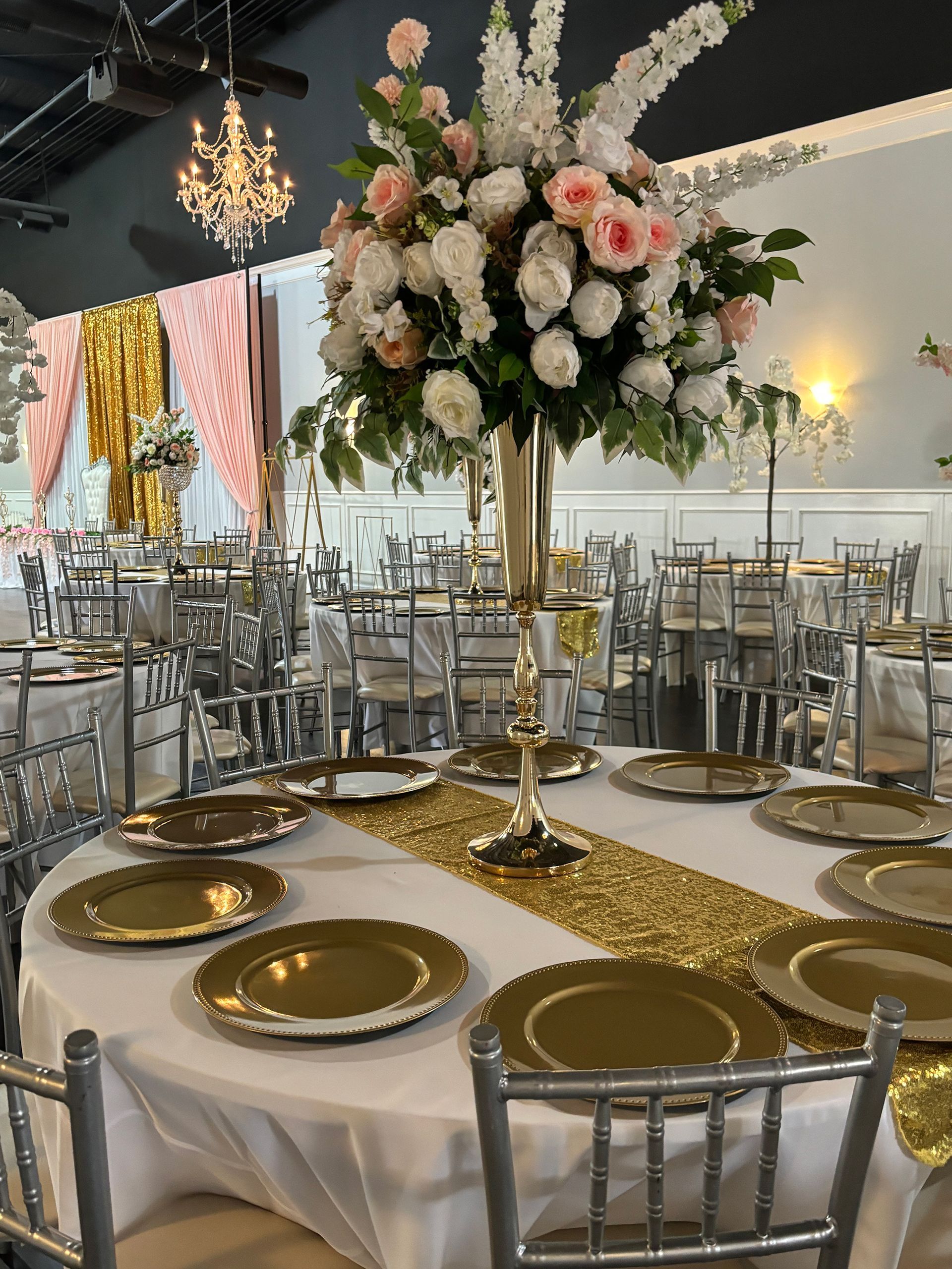 Formal event setting with round tables set for dining, silver chairs, floral centerpieces.