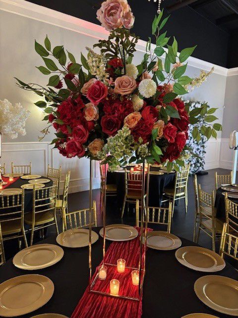 Elegant table setting with tall floral arrangement, red and gold accents, and black tablecloths.