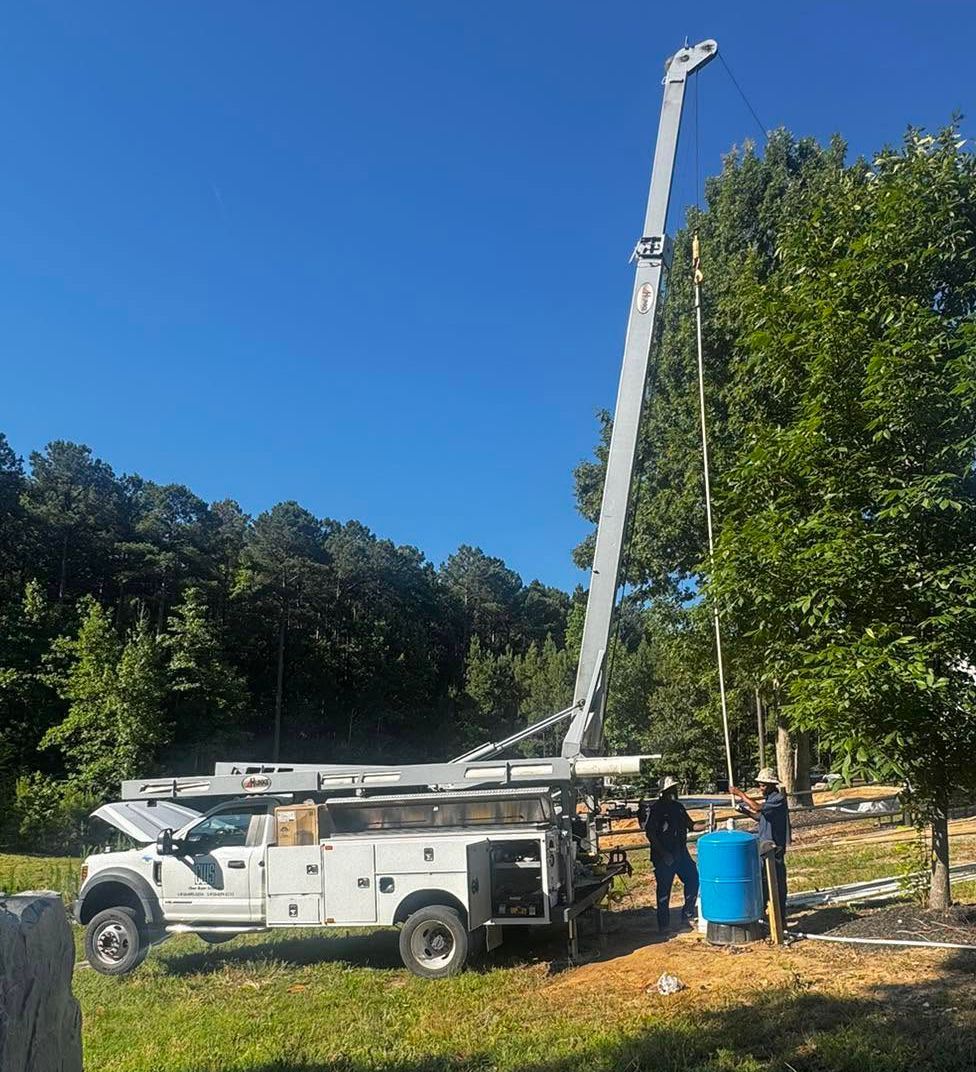 White utility truck with extended boom parked by trees and a blue barrel under a clear sky
