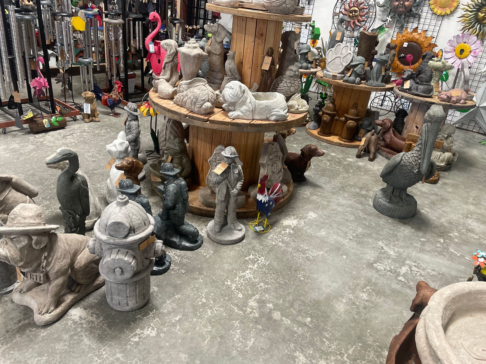 Outdoor display of assorted garden statues and stone figurines on tables and the ground