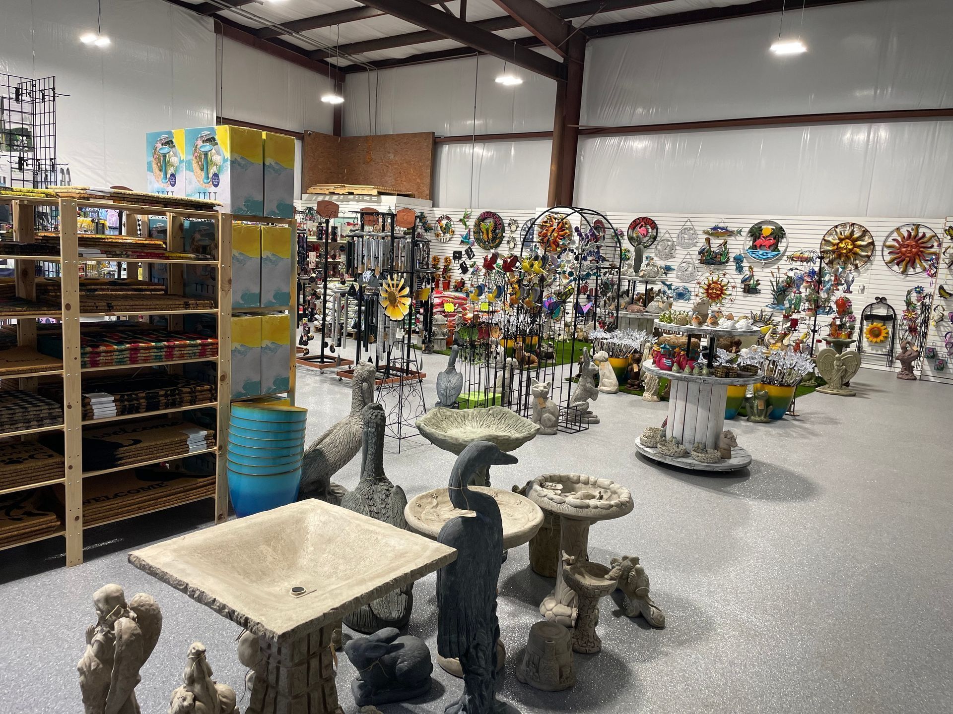 Indoor market aisle with shelves of decor, hanging ornaments, and stone garden stools on a concrete floor