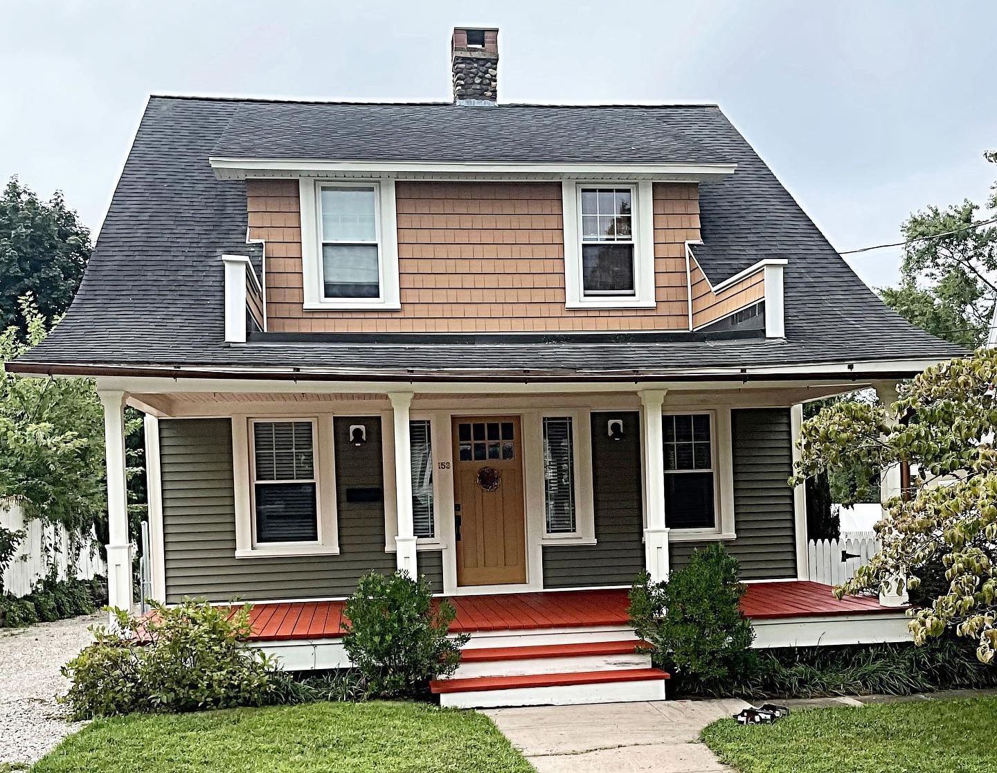 Two-story house with green siding, brown shingle facade, red porch, and small front yard with bushes.