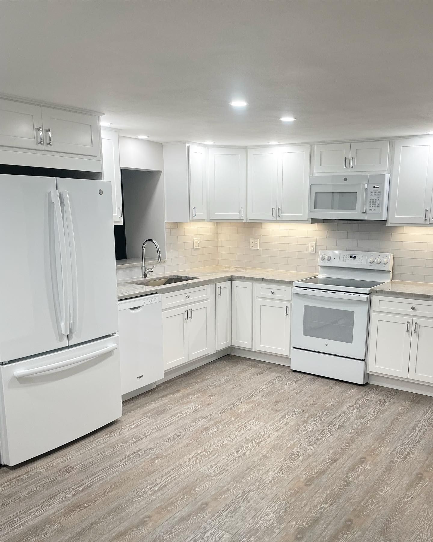 White kitchen with white appliances, cabinets, and light wood-look flooring.