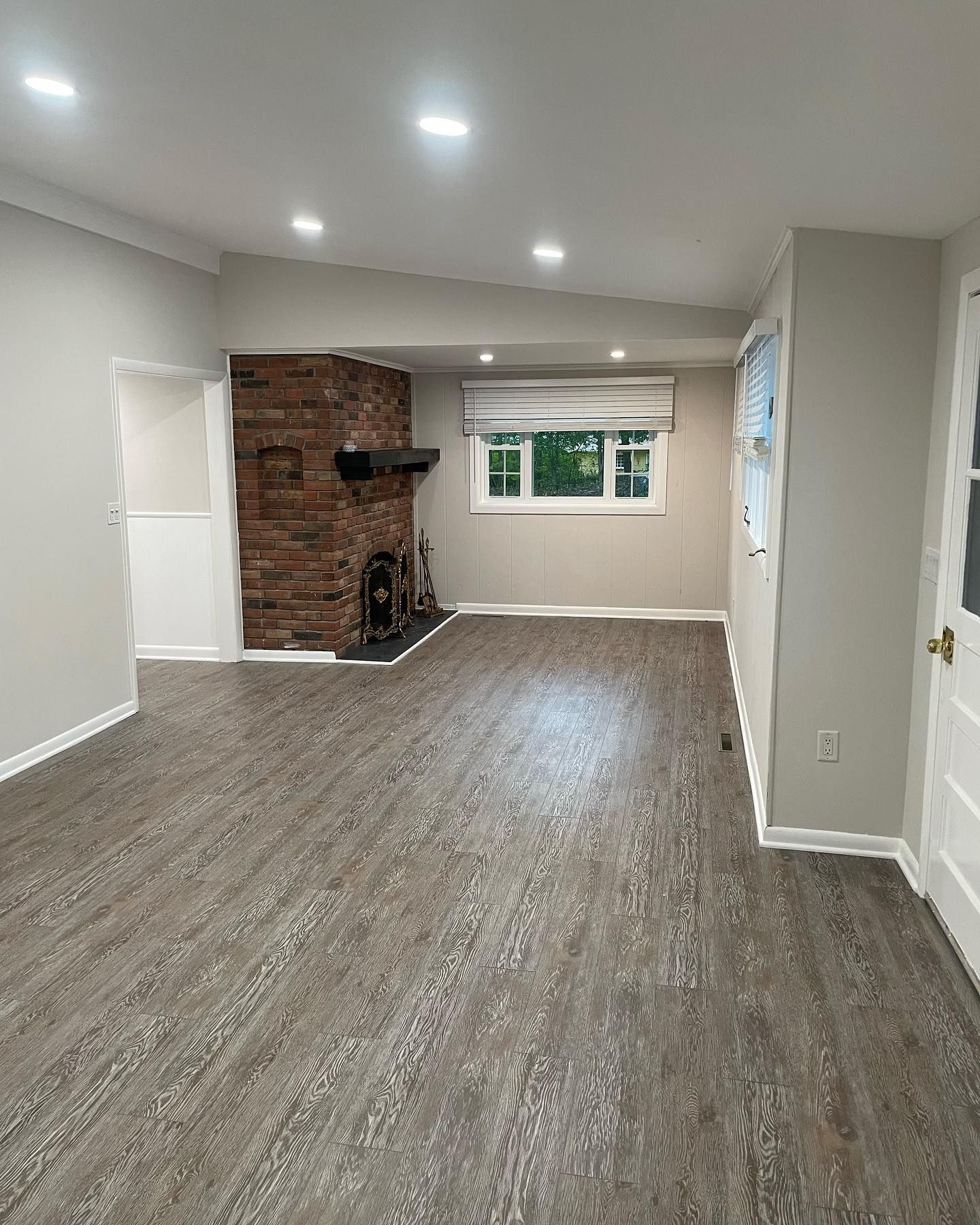 Empty living room with brick fireplace, gray walls, and wood-look flooring.
