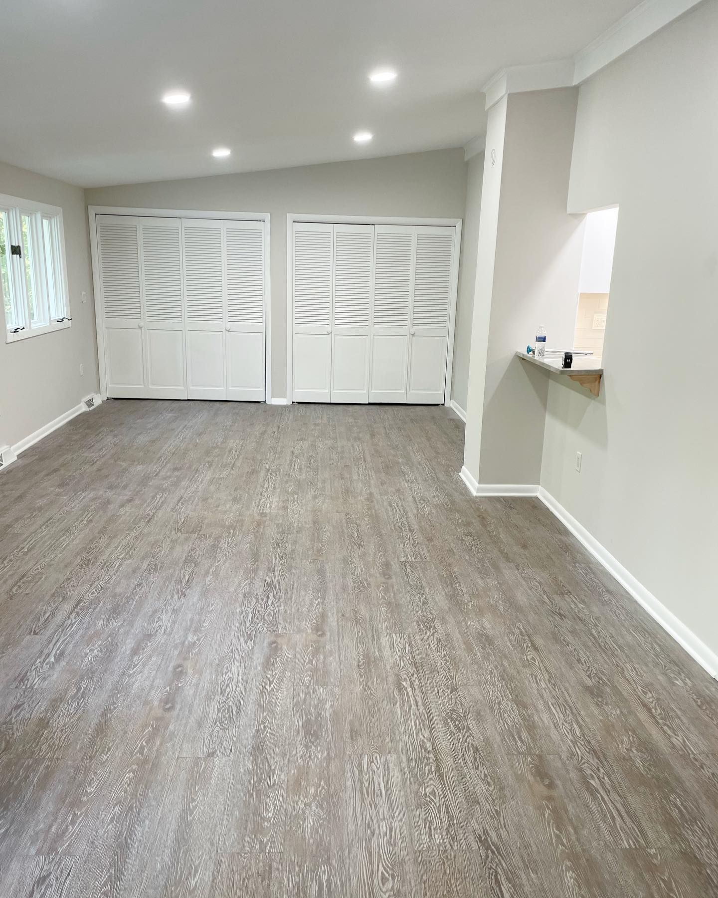 Empty room with gray wood-look flooring, white shutters, and recessed lighting.
