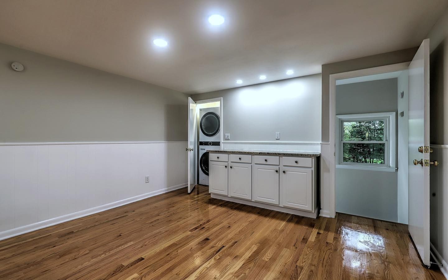 Laundry room with washer/dryer, white cabinets, hardwood floors, and open doorways.