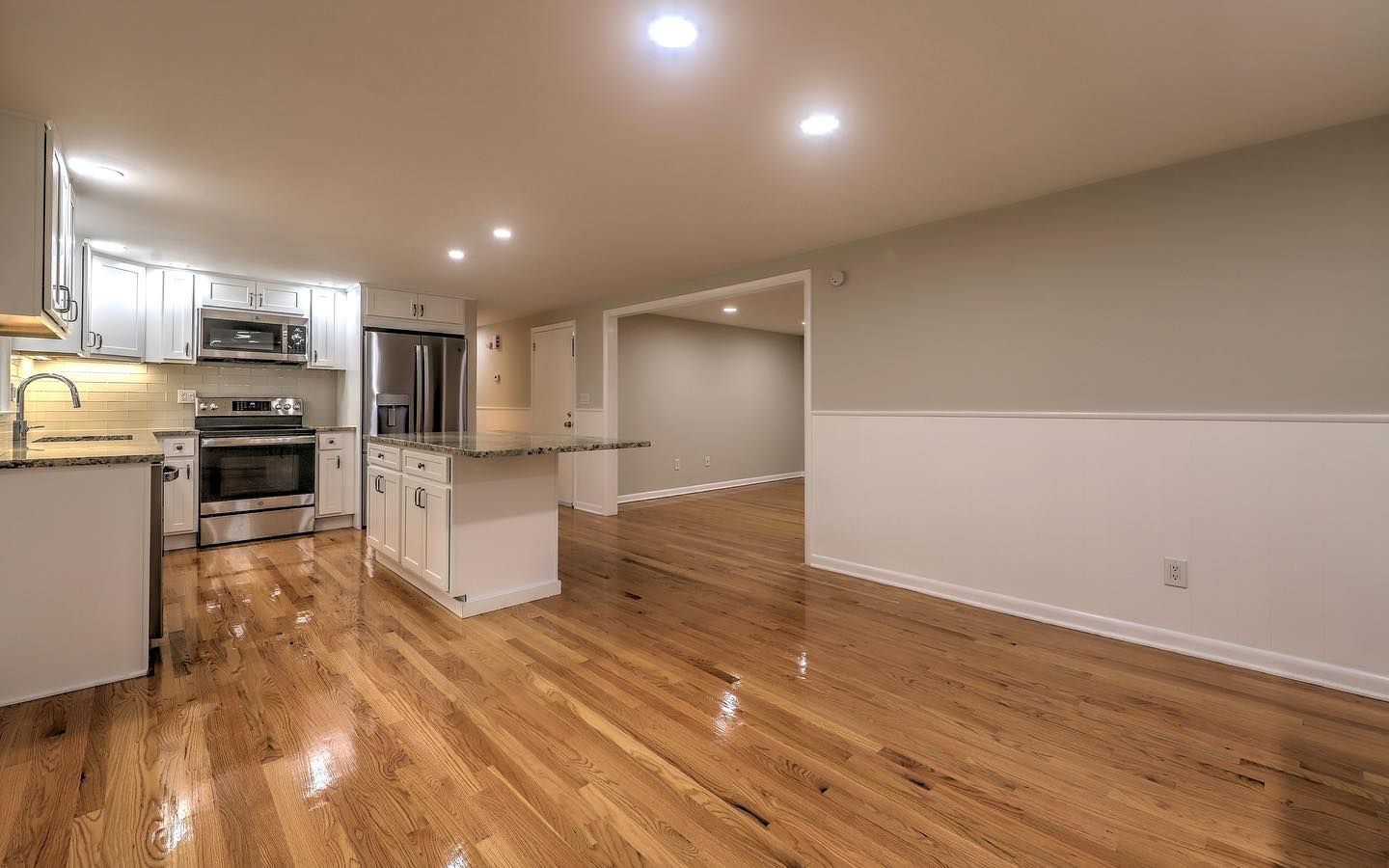 Kitchen with white cabinets, stainless steel appliances, and hardwood floors. Gray walls and doorway leading to another room.