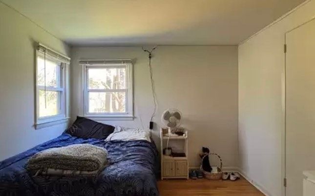 Bedroom with bed, windows, fan on nightstand, and closed door.