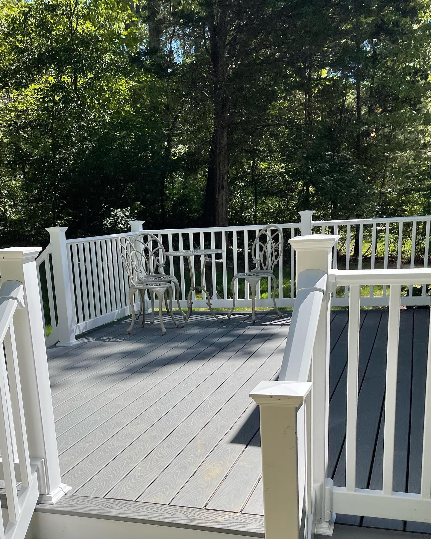 White deck with gray flooring, railing, and two metal chairs. Trees in the background.