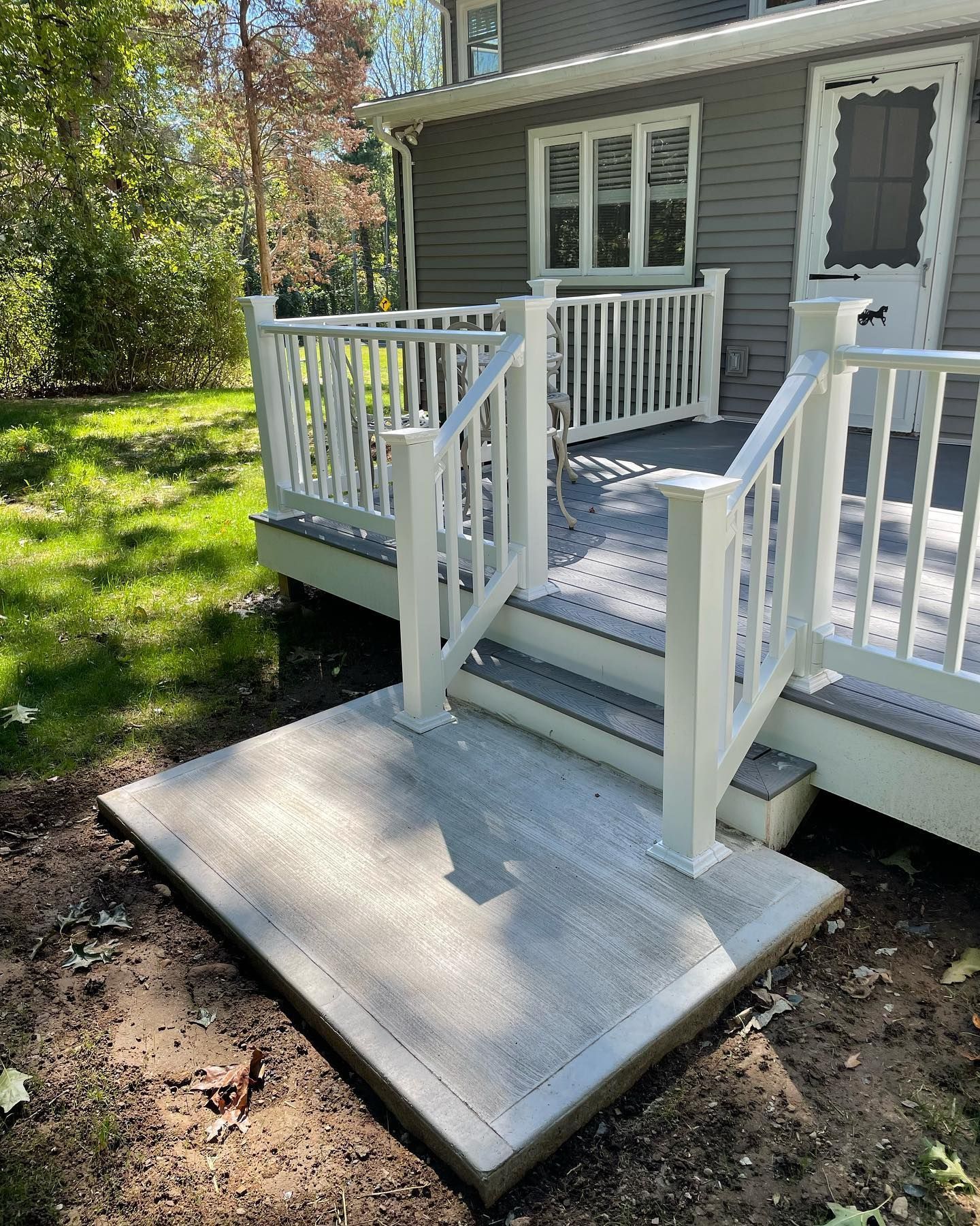 Gray composite deck with white railing and concrete landing in front of a house.