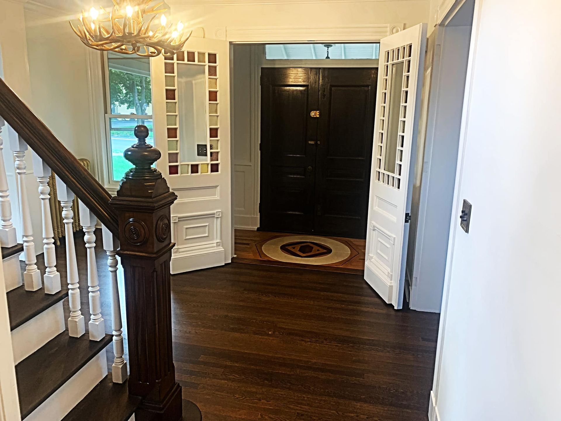 Entryway with staircase, dark wood floor, open doors, and chandelier.