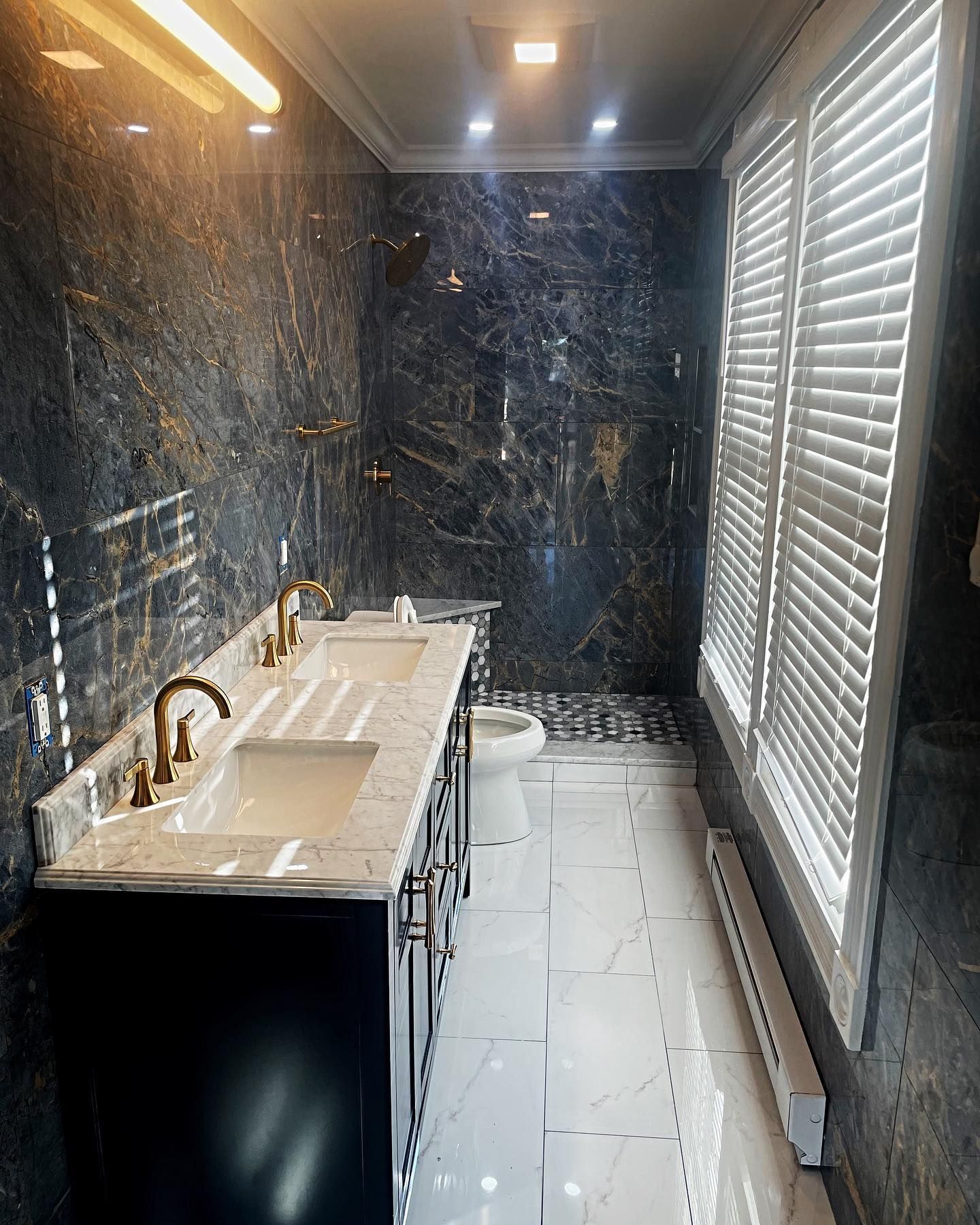 Luxurious bathroom with dark marbled walls, double vanity, and white shutters.