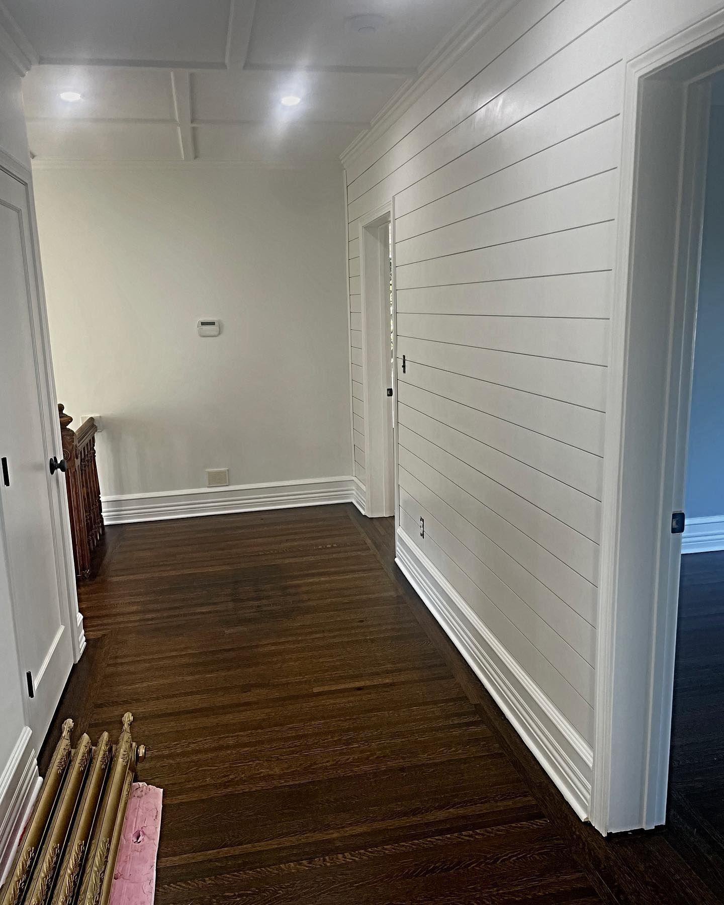 Hallway with dark wood floors, white walls (one with horizontal planks), and doorways.